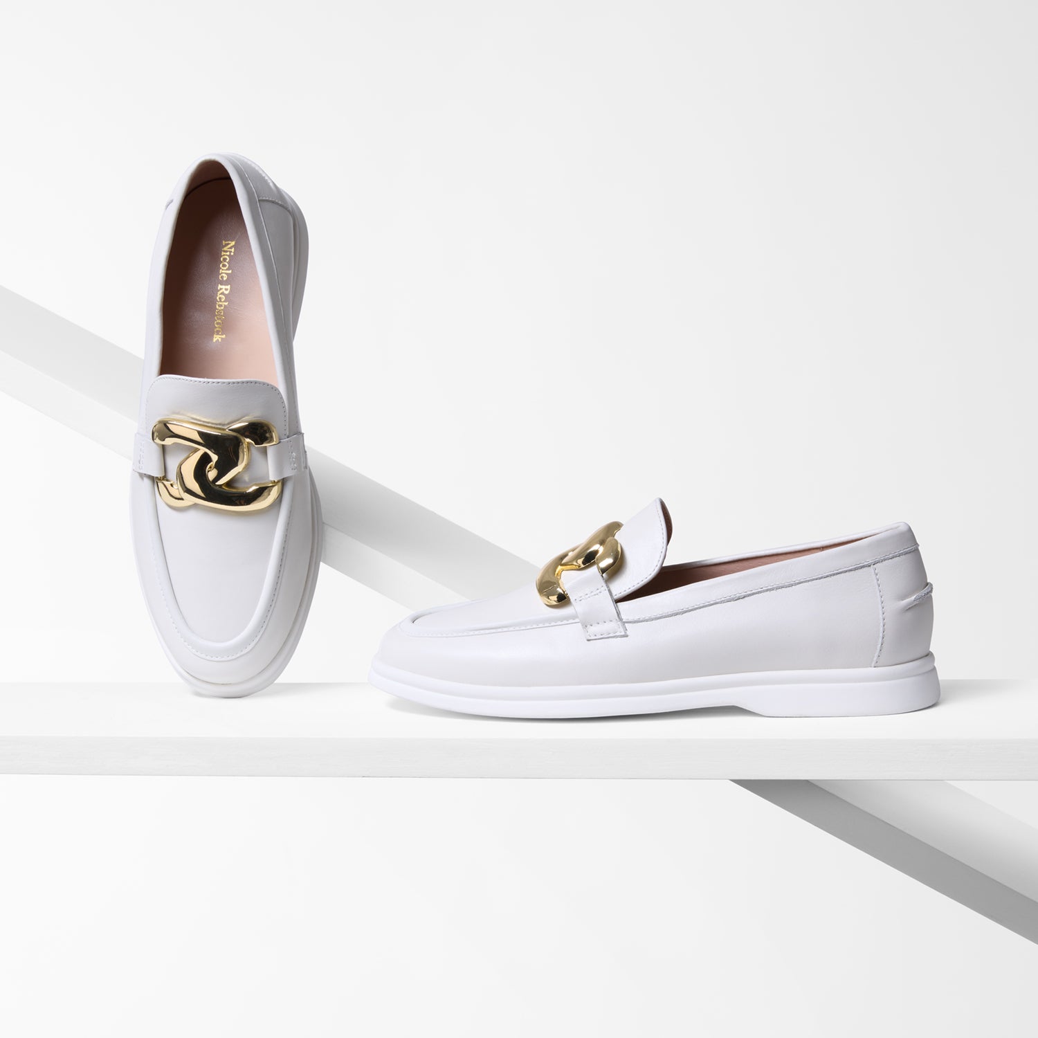 White loafers with gold buckles on a white background by Nicole Rebstock