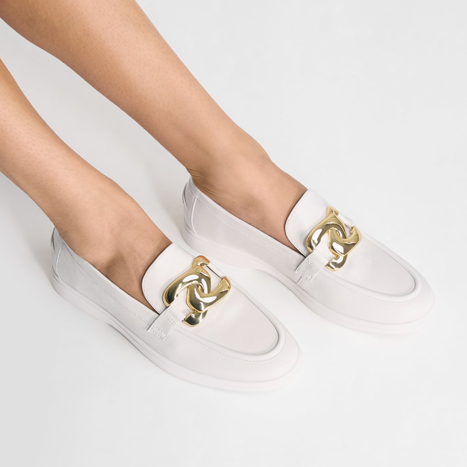White loafers with gold accents and almond toe worn by a person