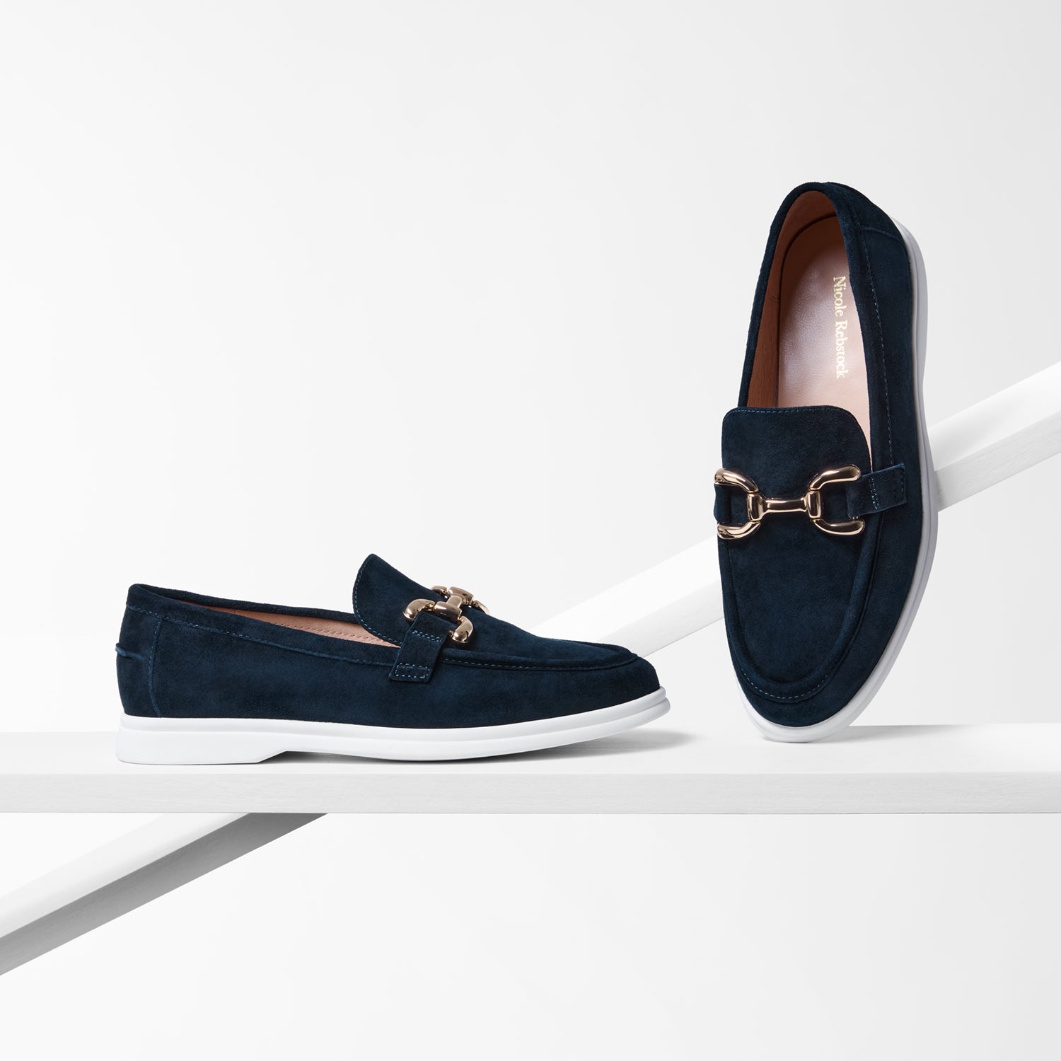 Navy loafers with gold accents and white sole on a white background