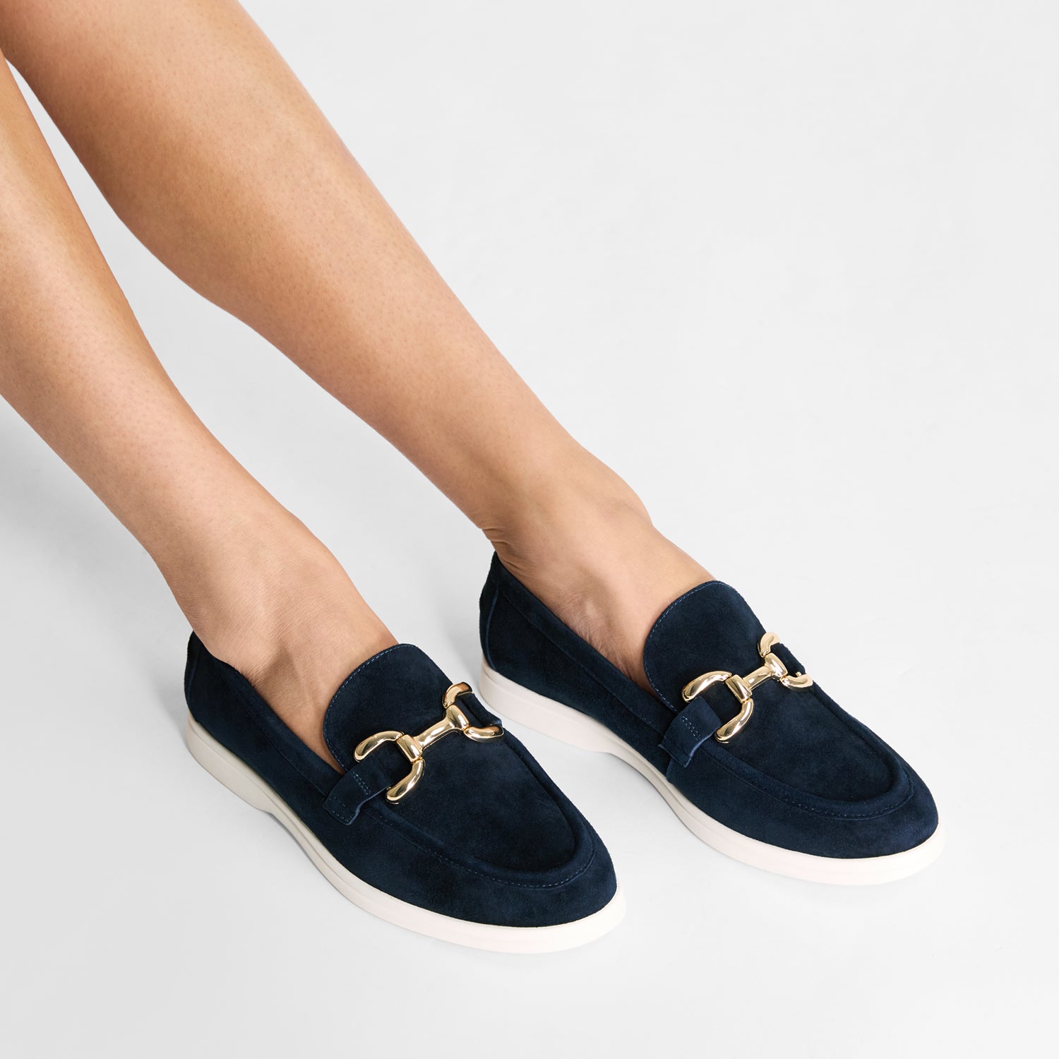 Navy boat inspired loafers with gold buckles worn by a person on a light gray background