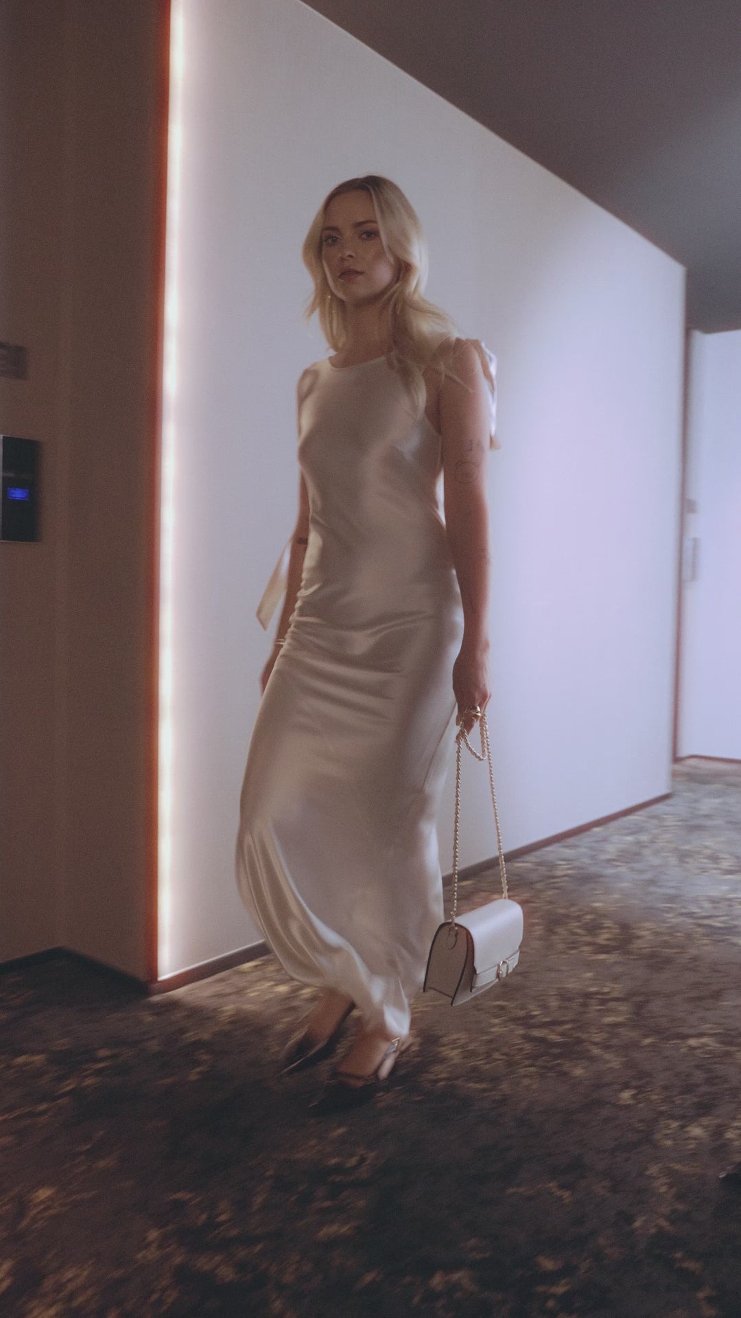 Video of model wearing Sevilla pinot noir patent slingblack with a silky ivory dress walking along a corridor.