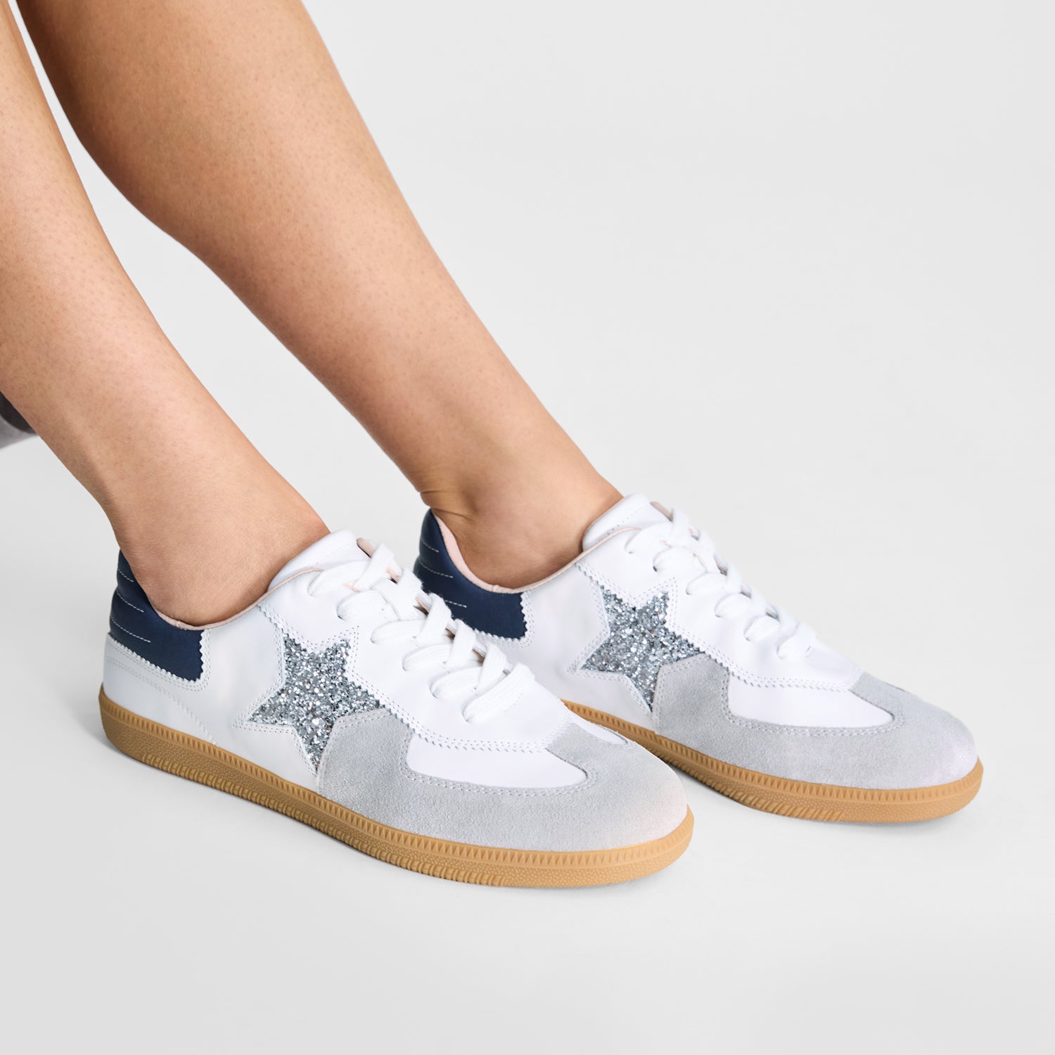 Nicole Rebstock's Amelia Sneaker. It's white with a brown sole with grey, silver and blue detailing.