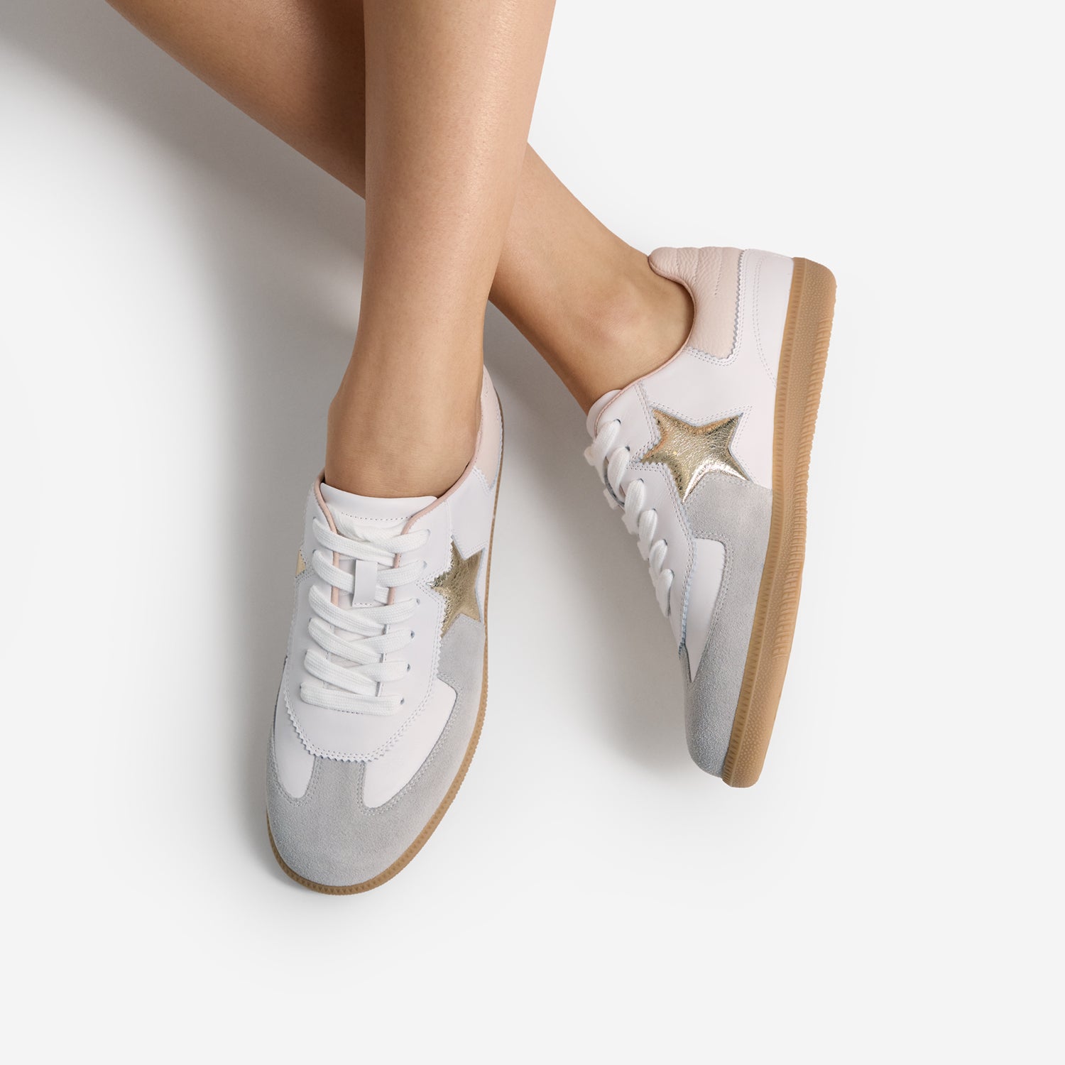 White sneakers with gold stars and grey suede and brown sole on a light grey background. By Nicole Rebstock.