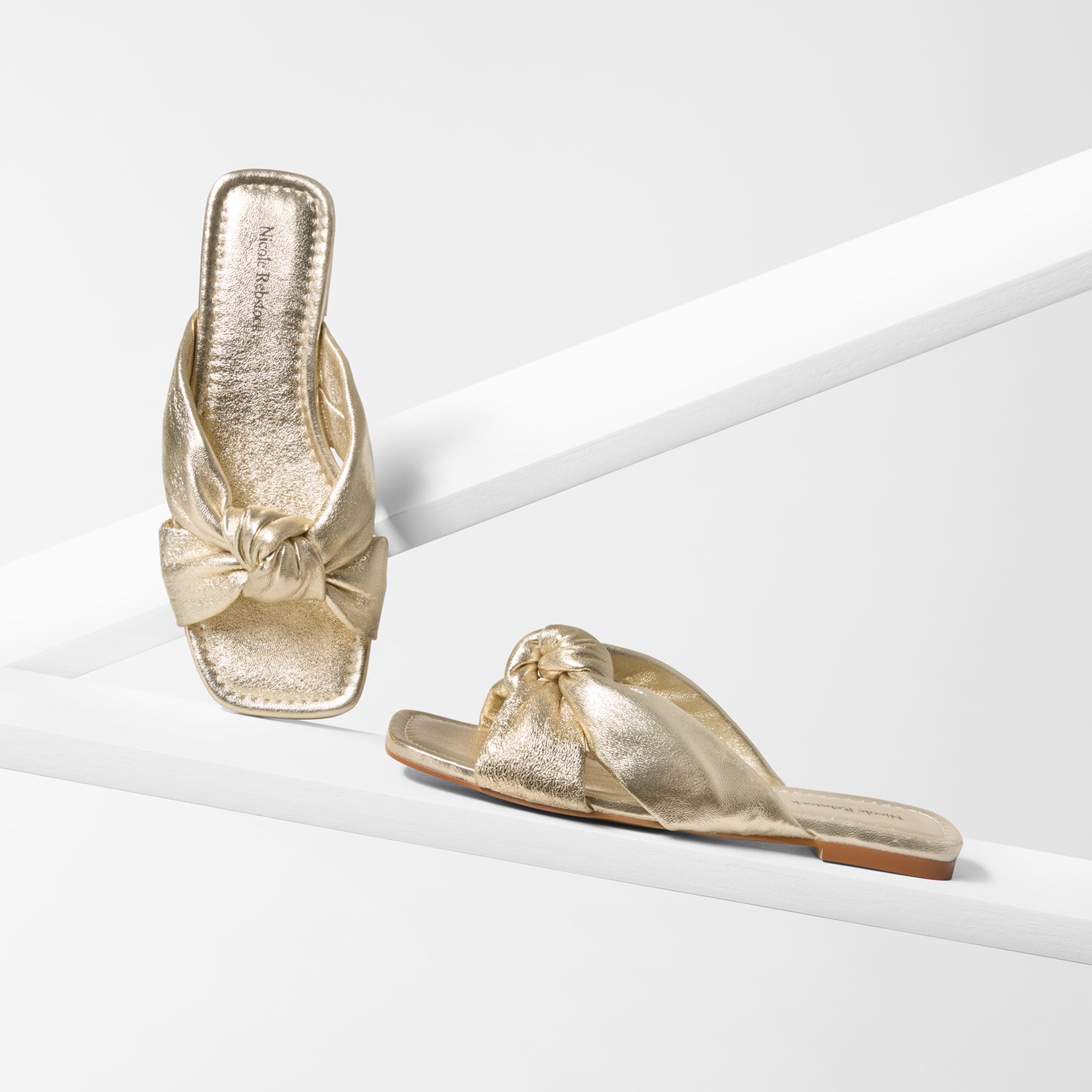 Gold sandals with a bow detail on a white background
