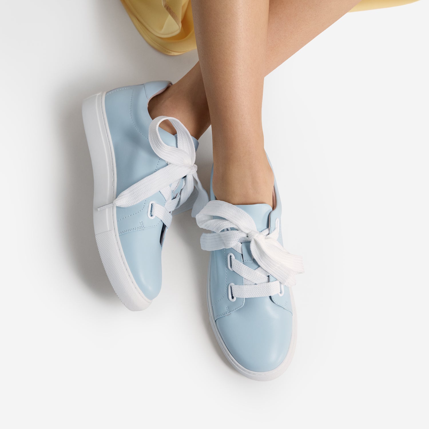 Light blue sneakers with white laces worn by a person on a light background