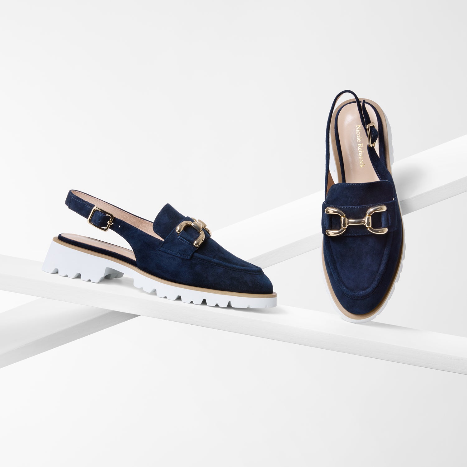 Navy blue slingback loafers with gold buckles on a white background by Nicole Rebstock