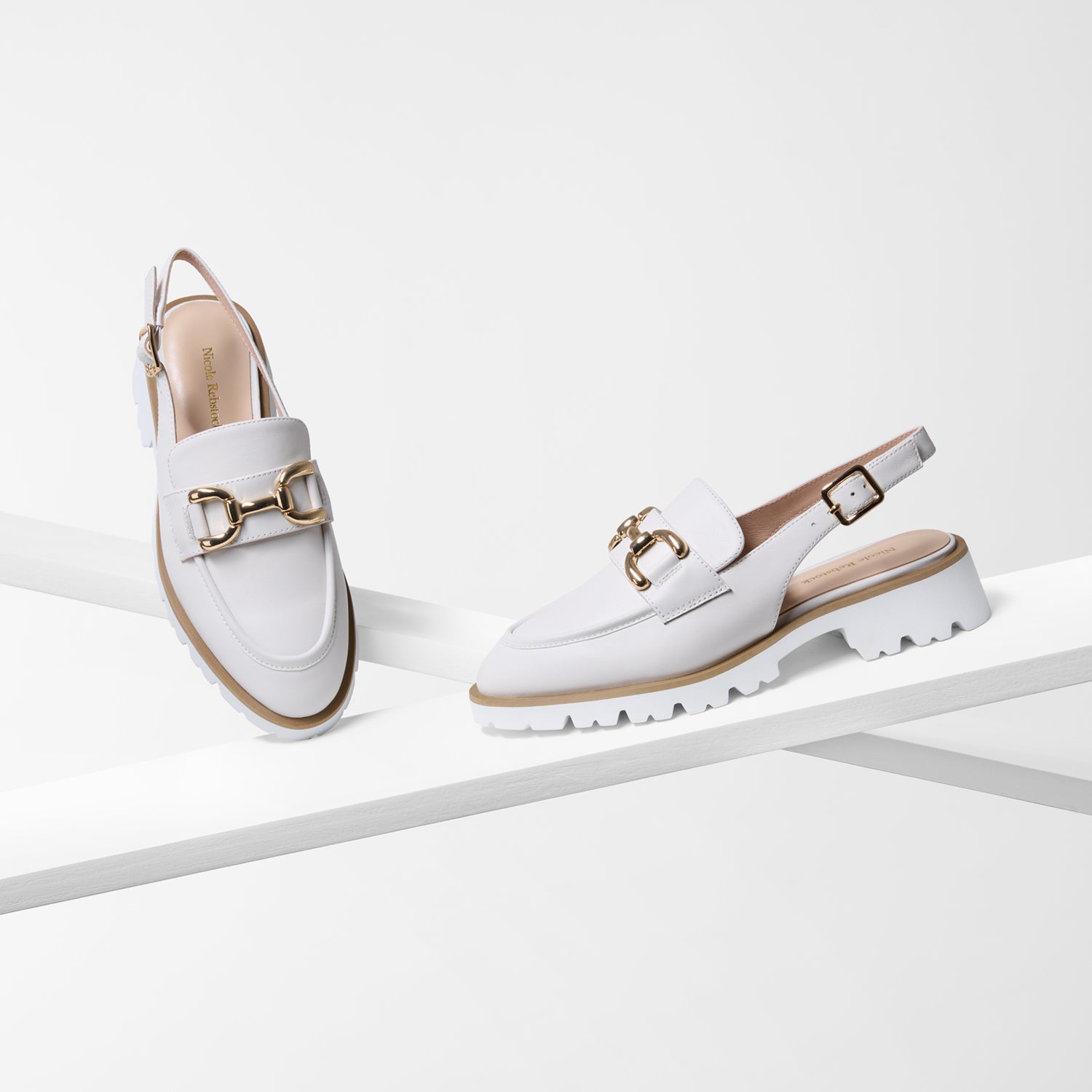 White chunky loafers with gold buckles on a white background