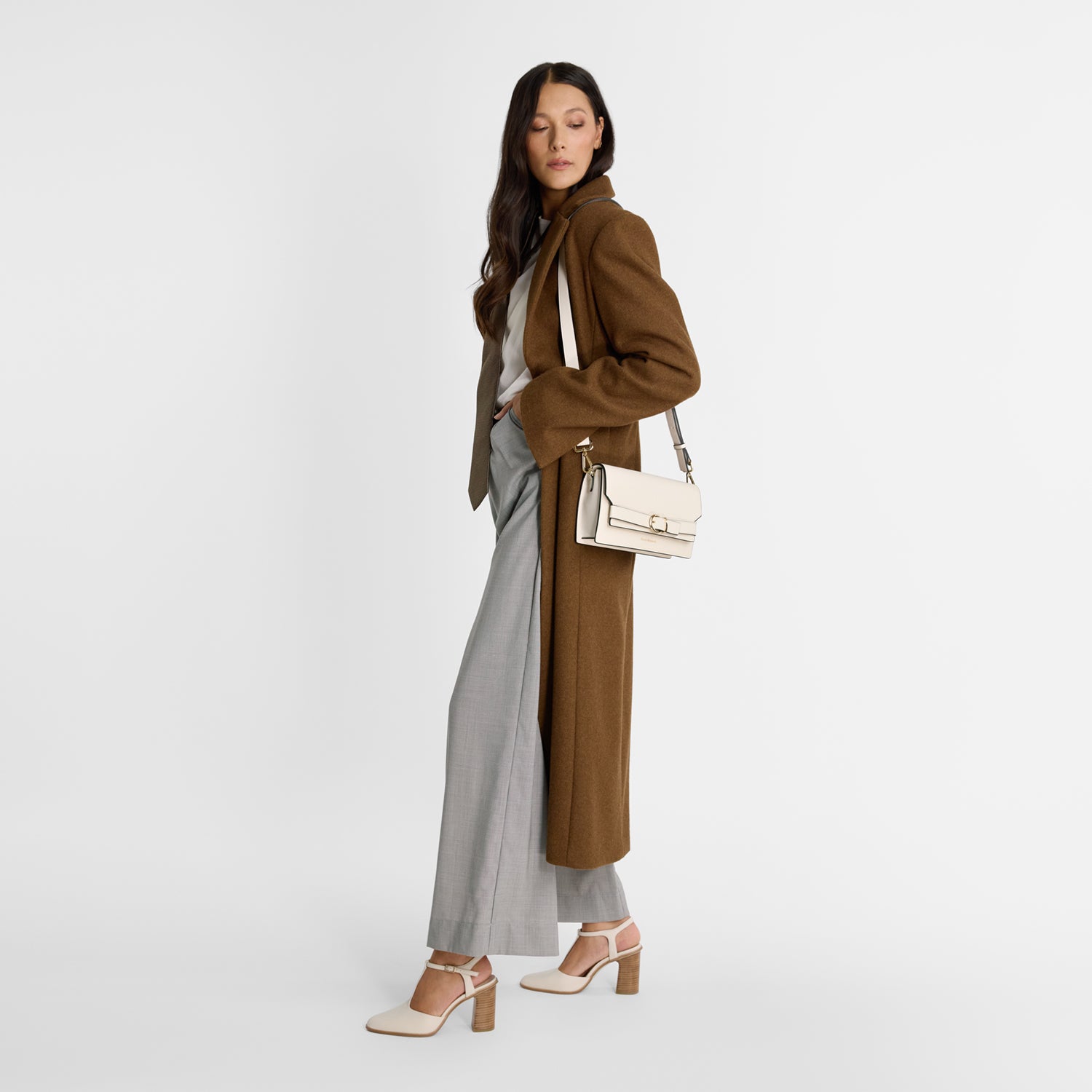 Woman wearing ivory T-bar pumps with wooden heel. Almond toe, leather. Gold buckle.