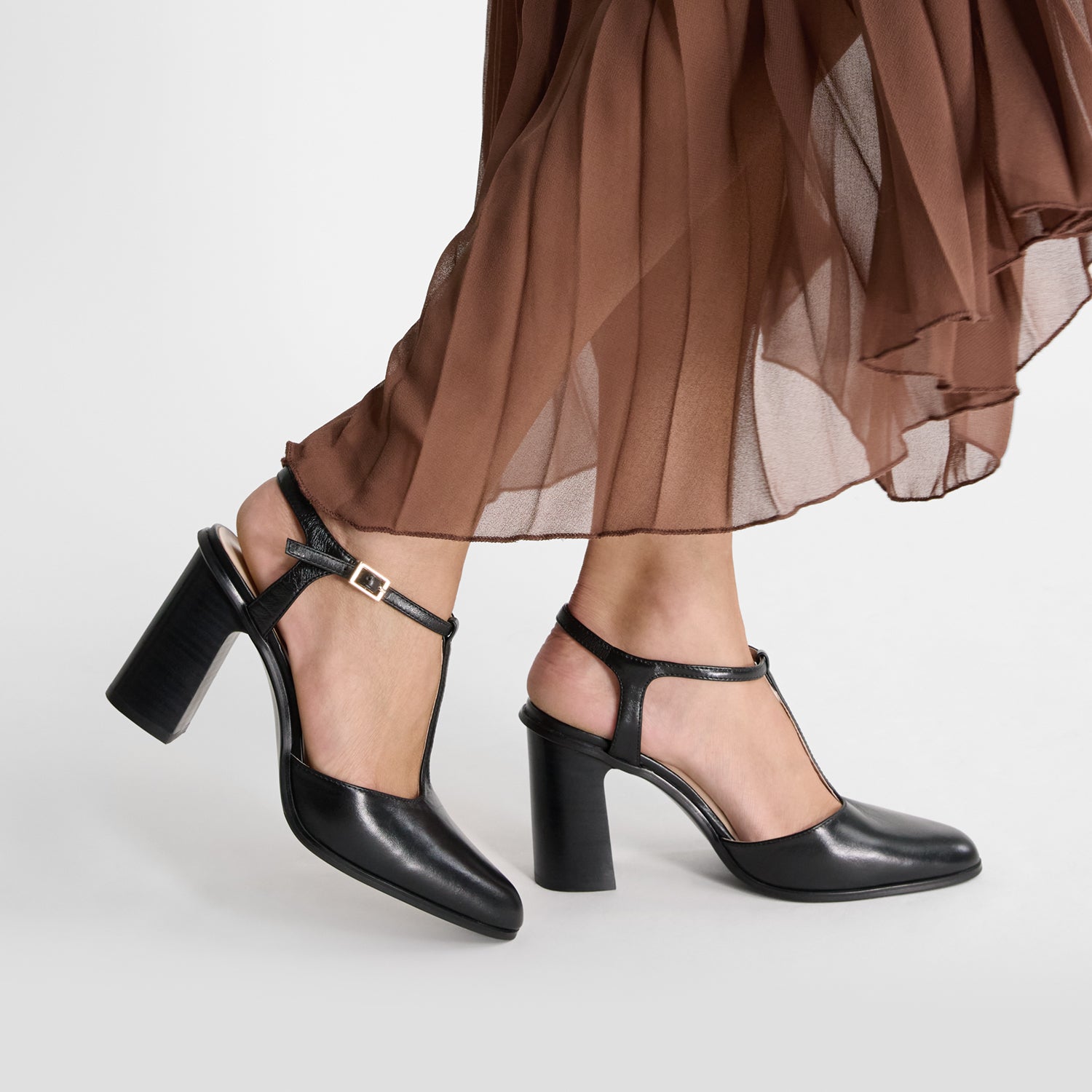 Black block high-heeled shoes worn by model with t-bar and almond toe.