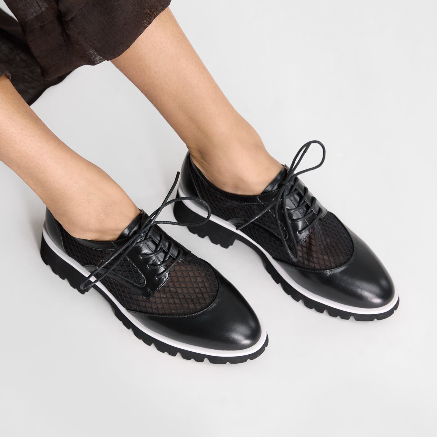 Black leather shoes with textured panels worn by a person on a light grey background. Made by Nicole Rebstock.