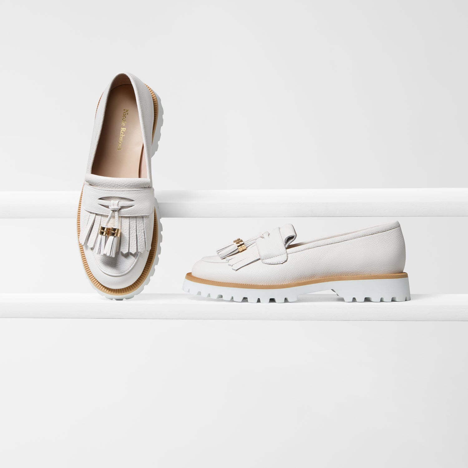 A pair of white leather loafers with tassel details and gold-tone hardware, displayed on a clean white studio background.