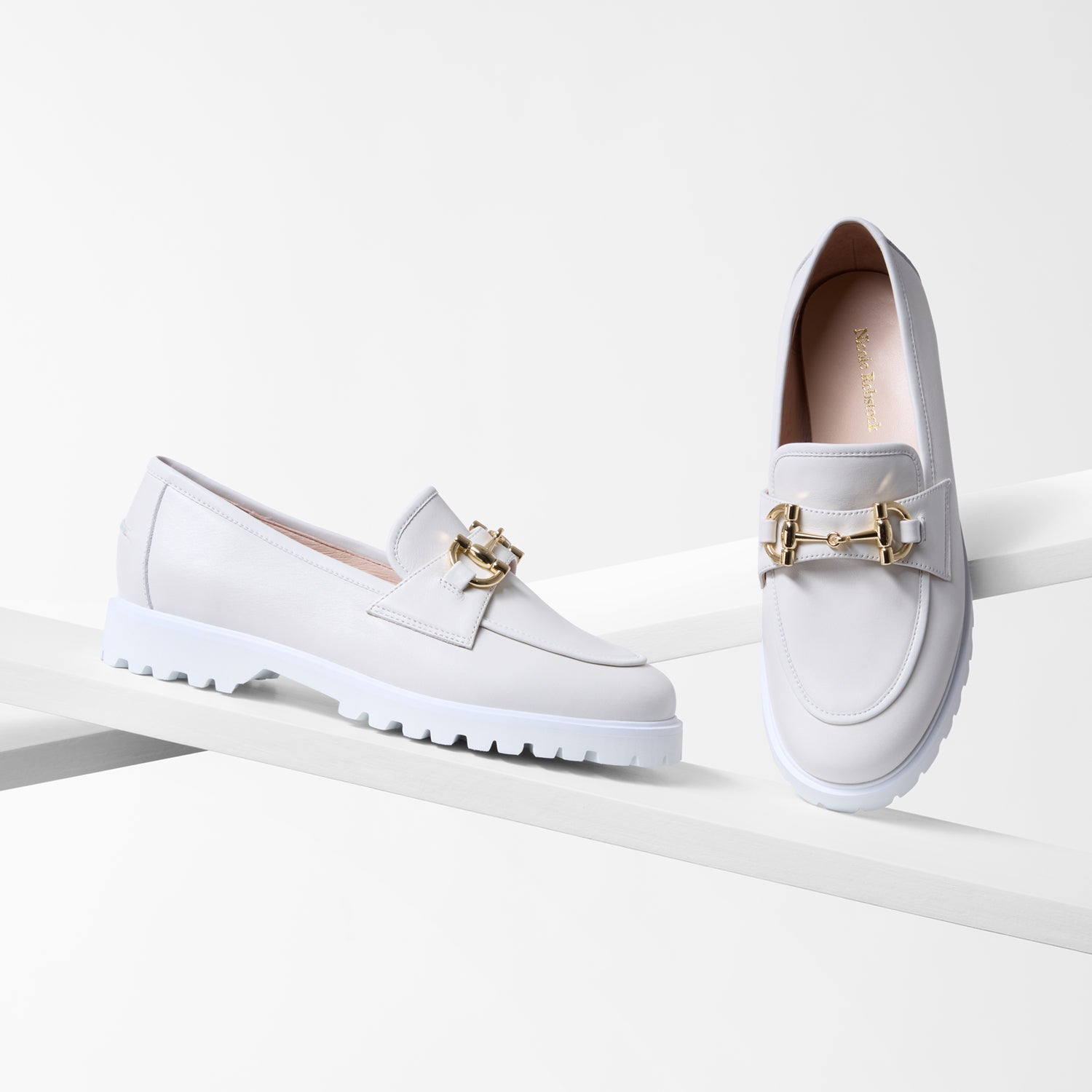 White loafers with and almond toe and gold buckles on a white background