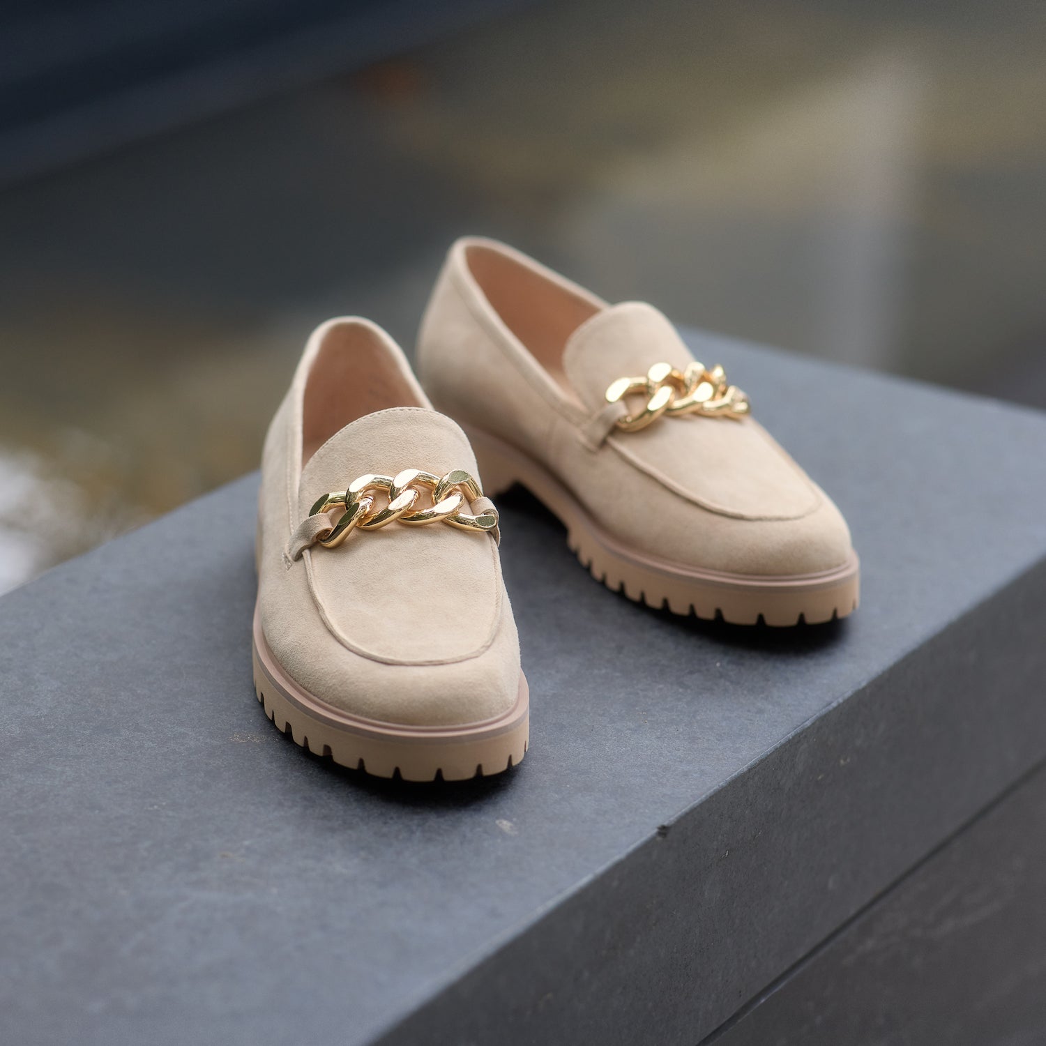 Nude suede loafers with gold chain details on a dark surface