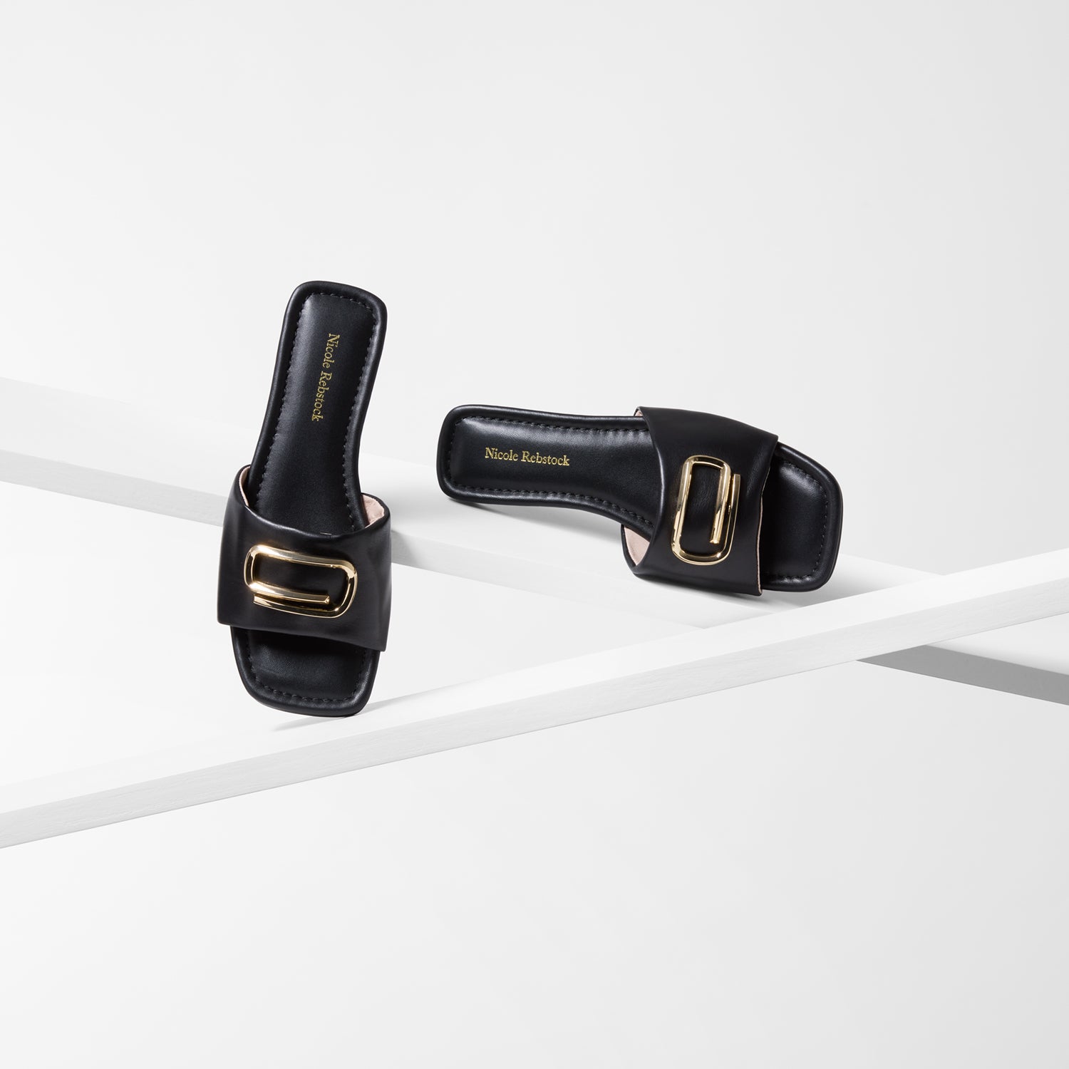 Black sandals  by Nicole Rebstock with gold buckles on a white background