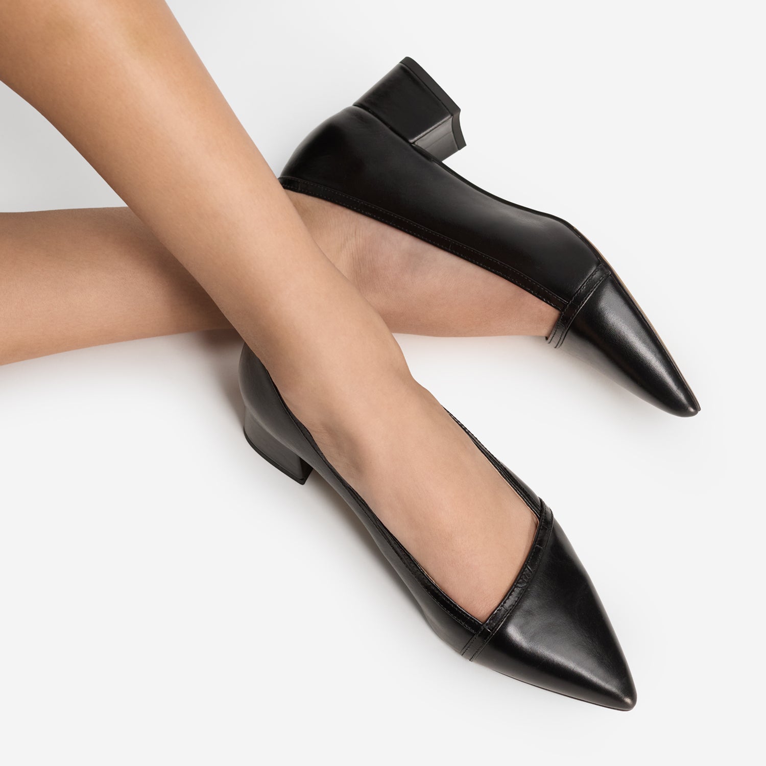 Black pointed-toe shoes worn by model up close with black croc print trim and angled cut