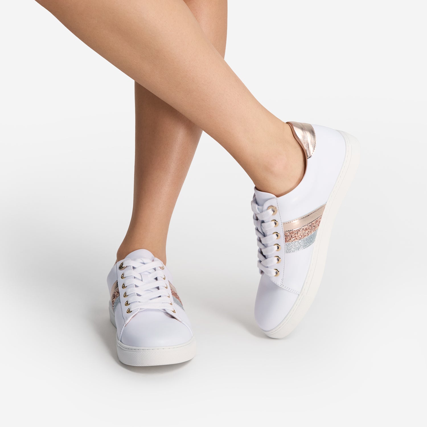 White sneakers with rose gold and silver accents worn by a person on a white background