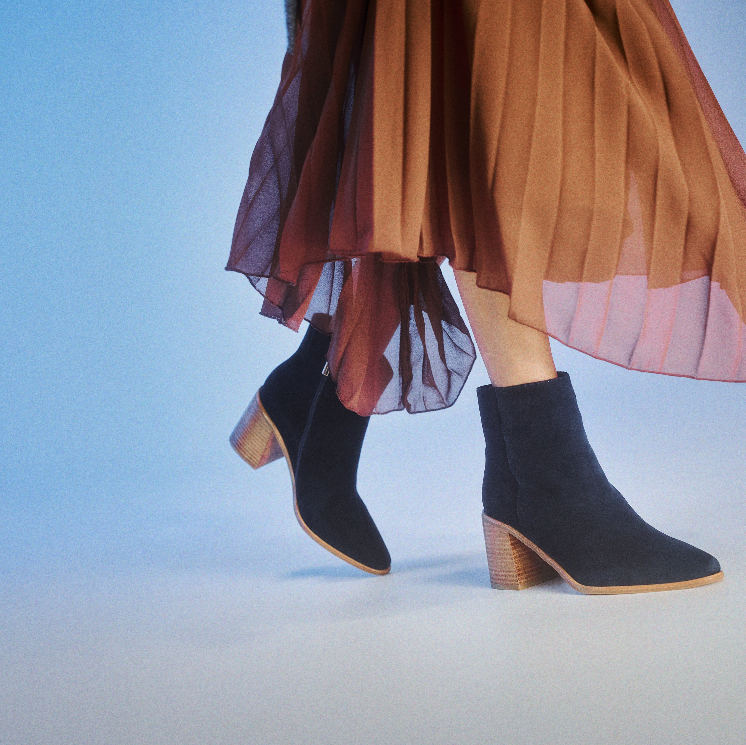 Navy ankle boots with stacked leather heel worn with a brown skirt on a light blue background