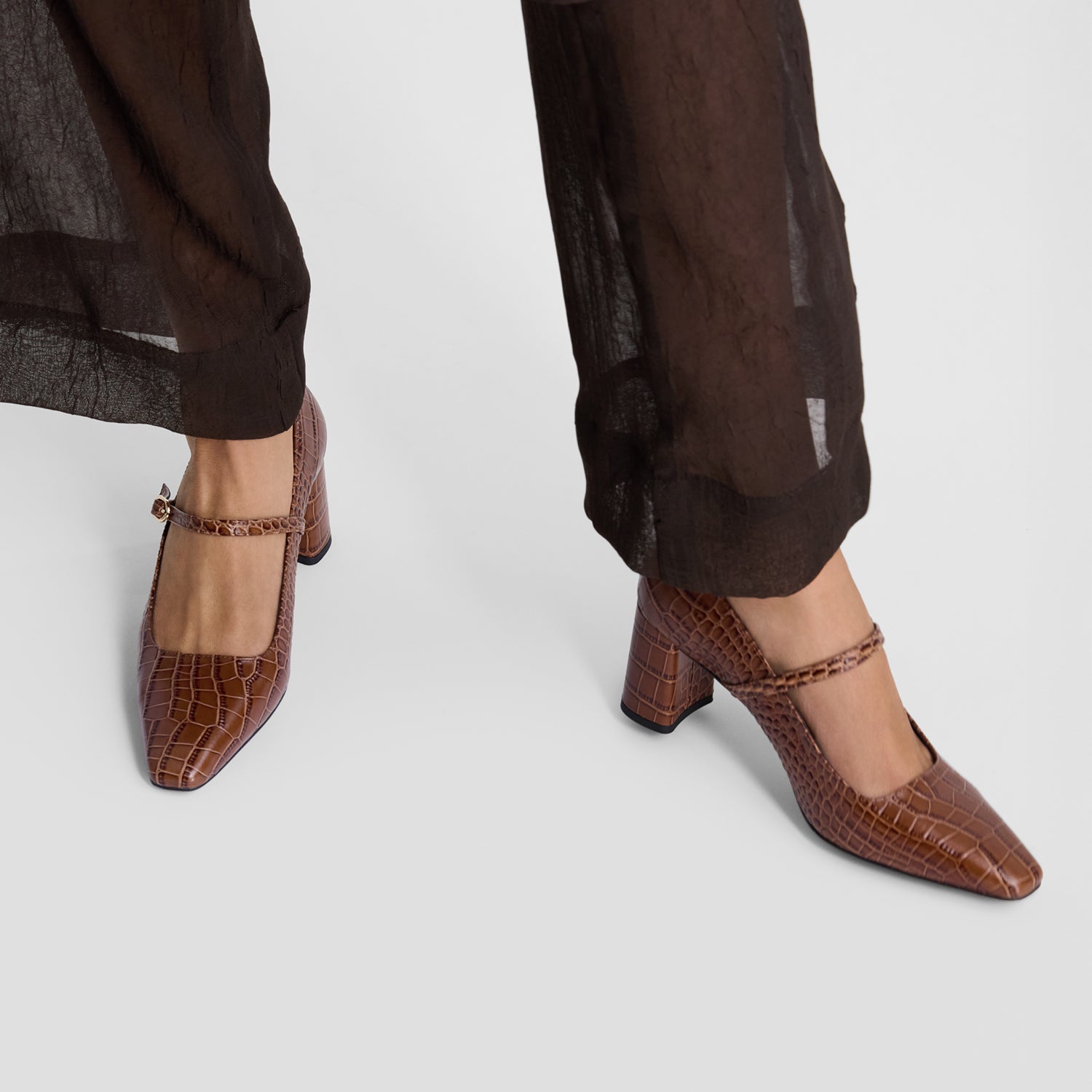 Brown crocodile-patterned high-heeled shoes on a light gray background