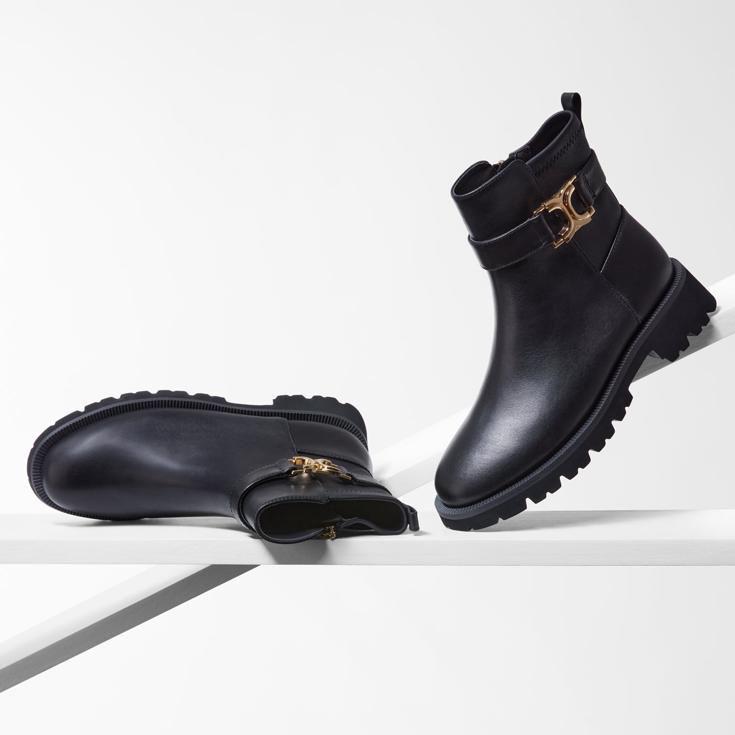 Black ankle boots with gold buckles on a white background.
