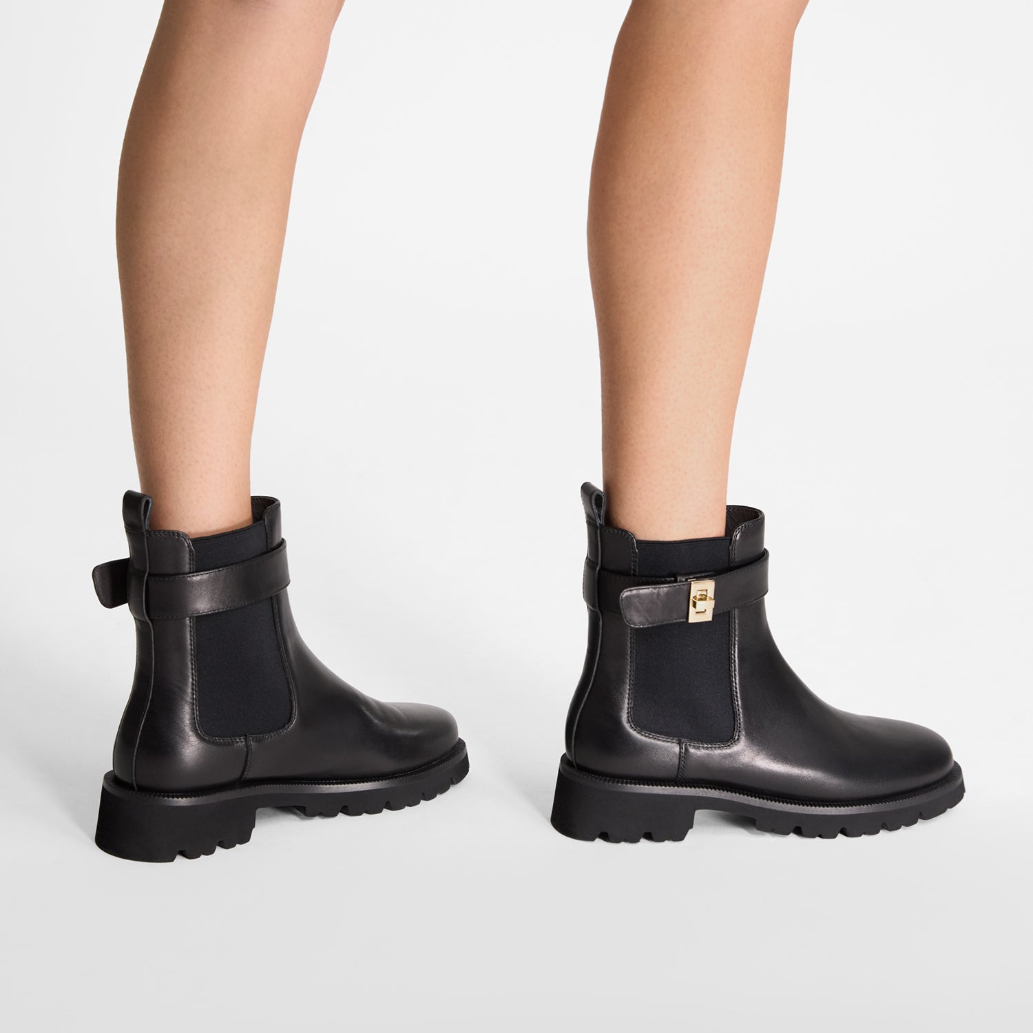 Black ankle boots with a chunky sole, strap with gold buckle on a white background
