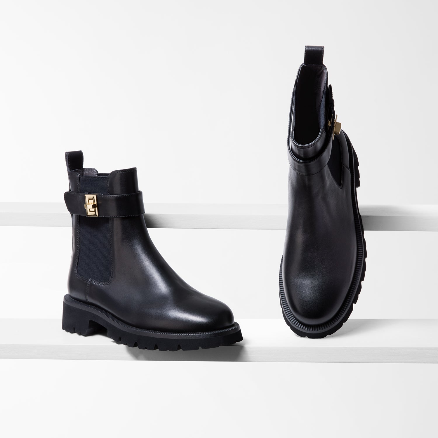 Pair of black leather boots with gold buckles on a white background