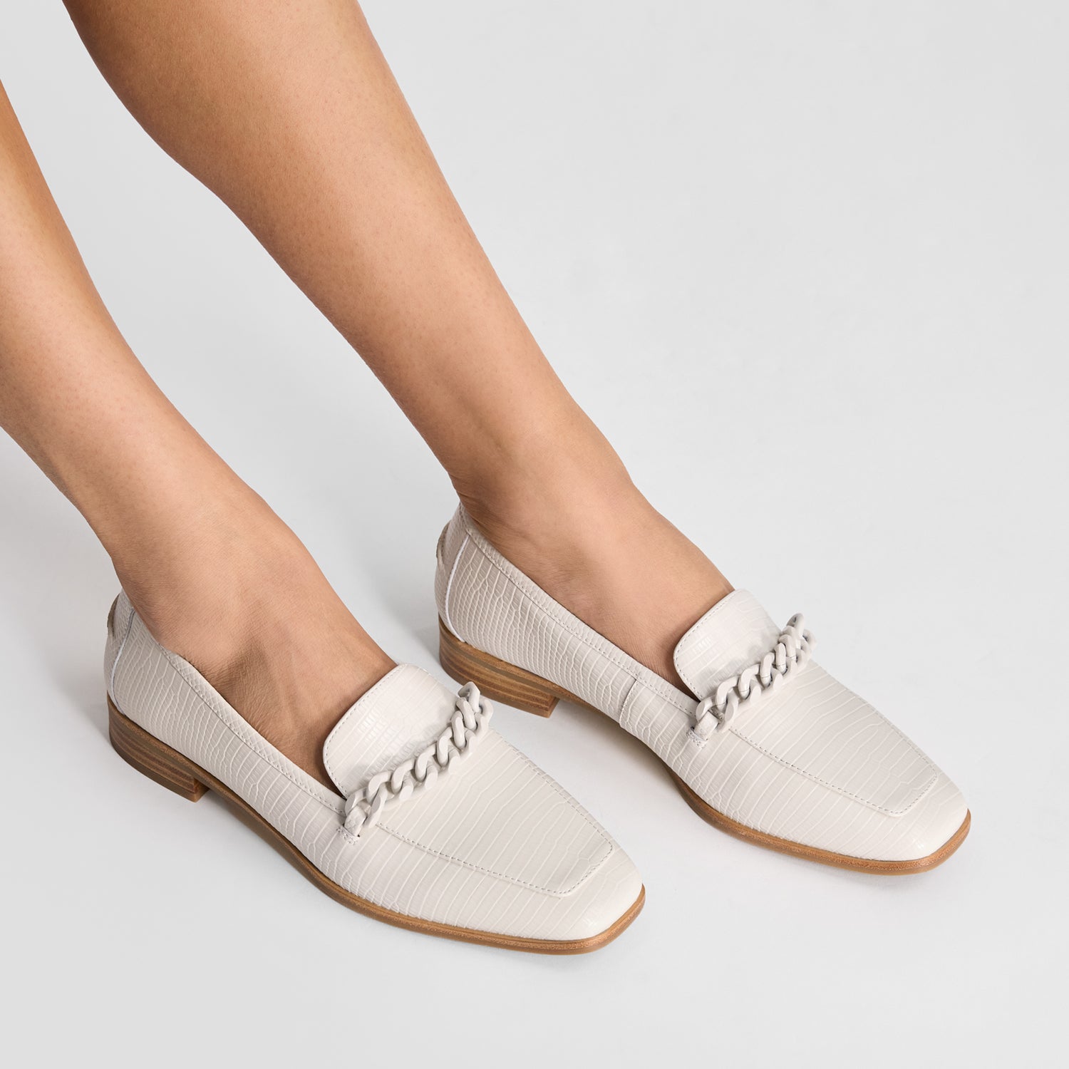 Ivory loafers with brown soles worn by a person on a light gray background