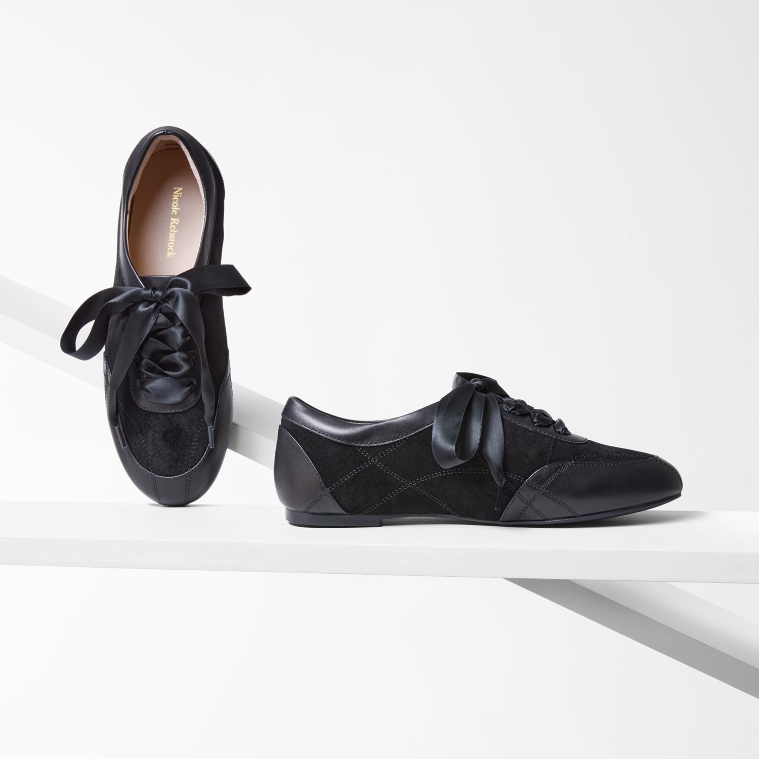 Pair of black sneakerinas with bow details on a white background