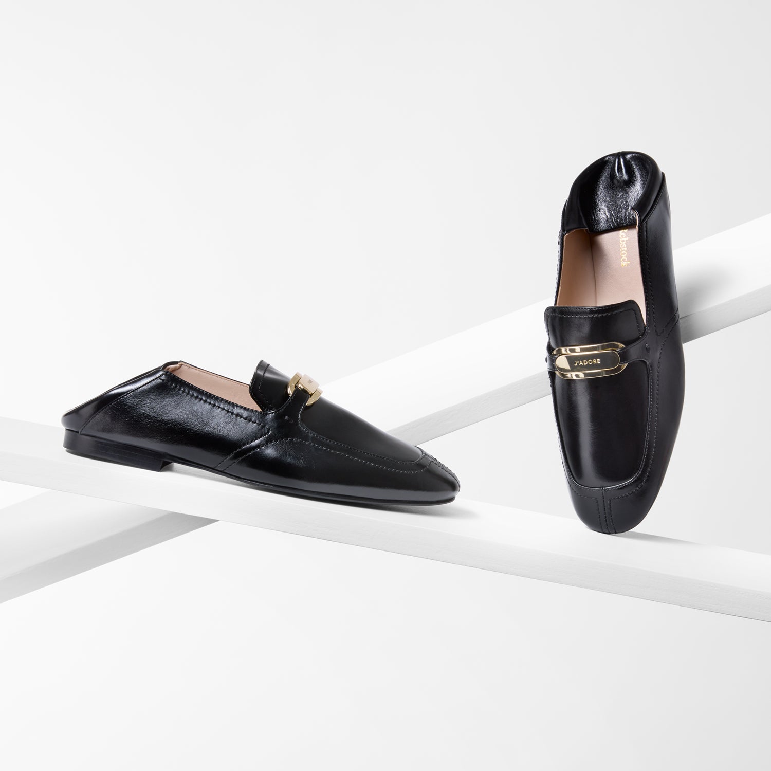 Black loafers with gold accents on a white background