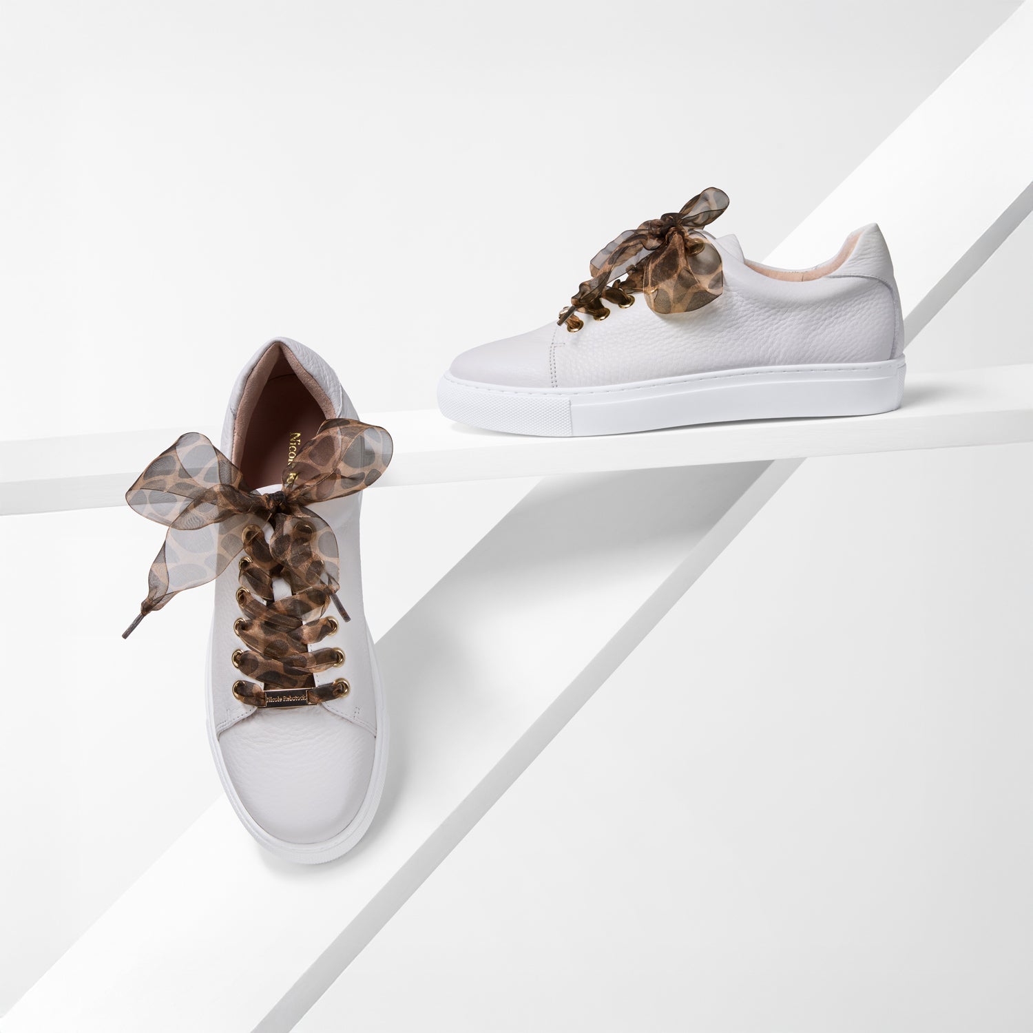 White sneakers with decorative leopard print laces on a white background