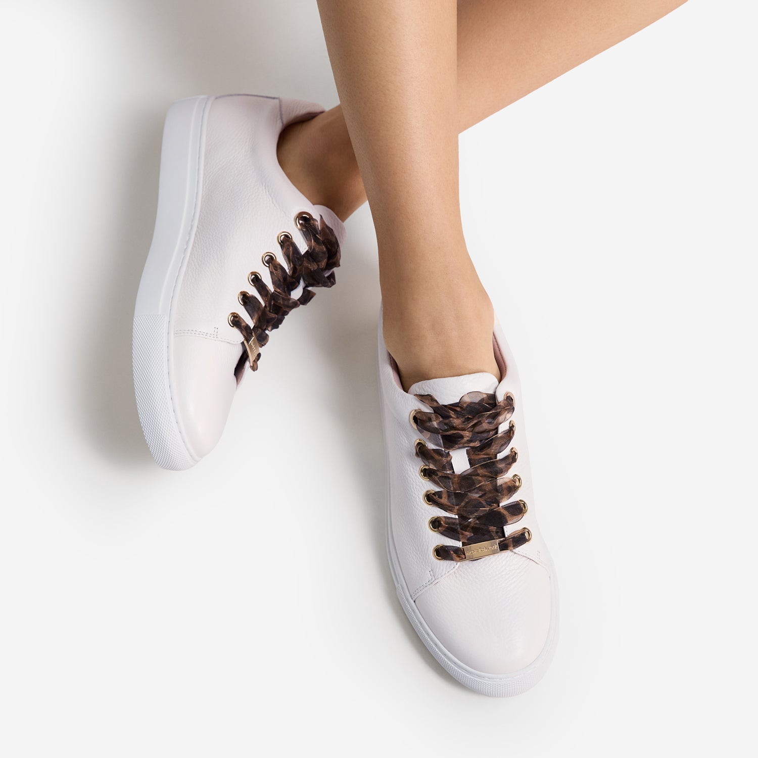 White sneakers with leopard laces worn by a person on a light gray background