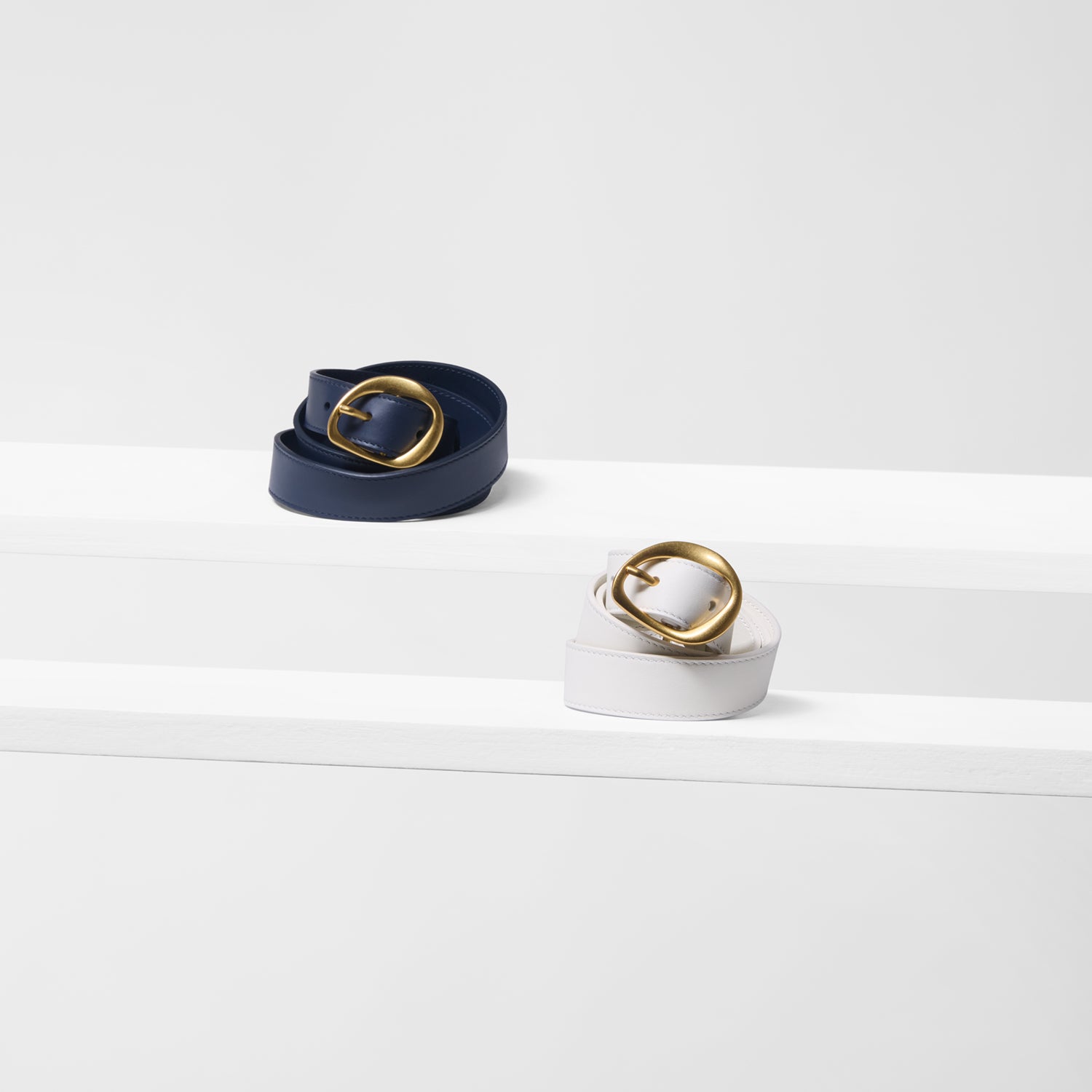 Two belts, one navy and one white, with gold buckles on a white background