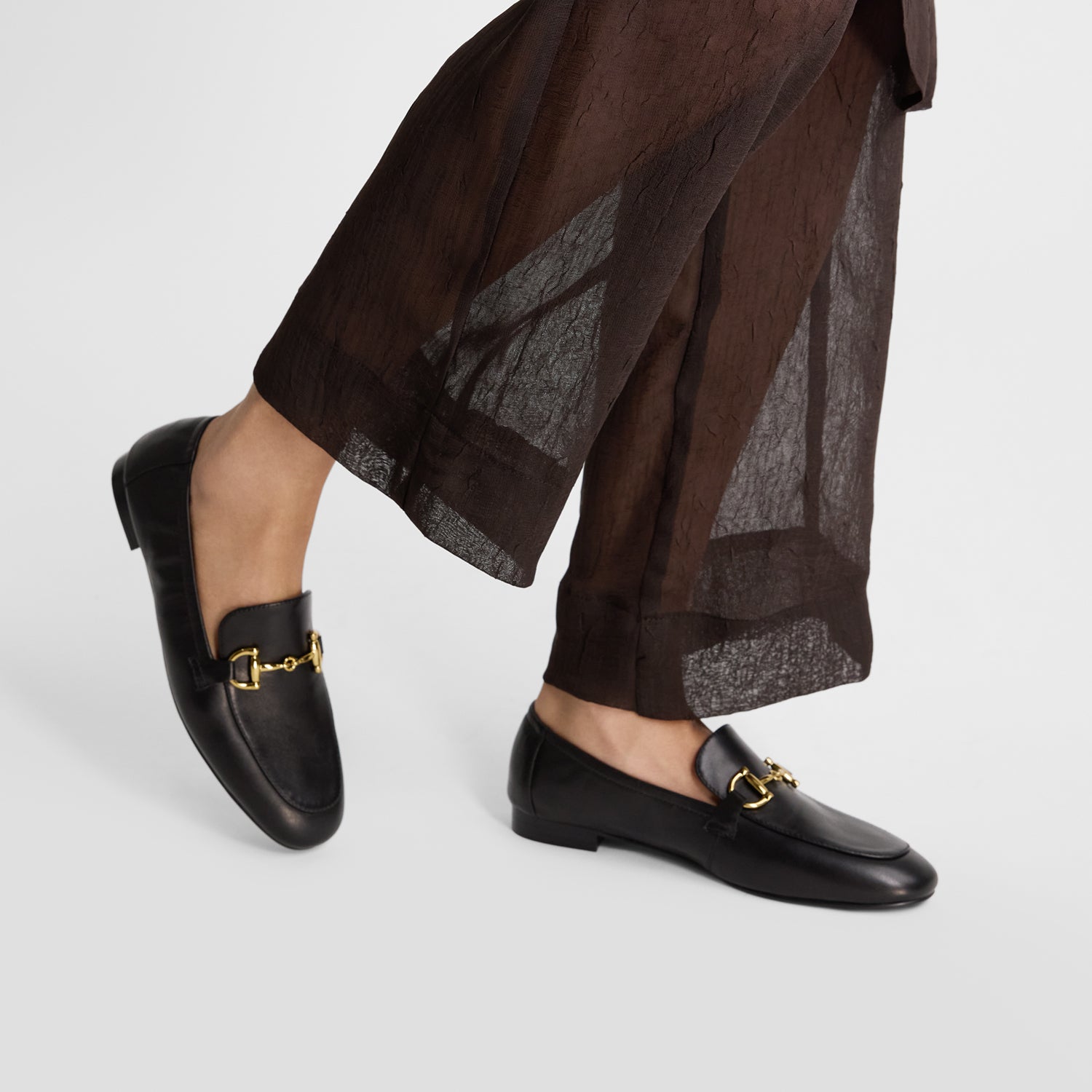 Flat black leather loafers with an elastic back worn by a model.