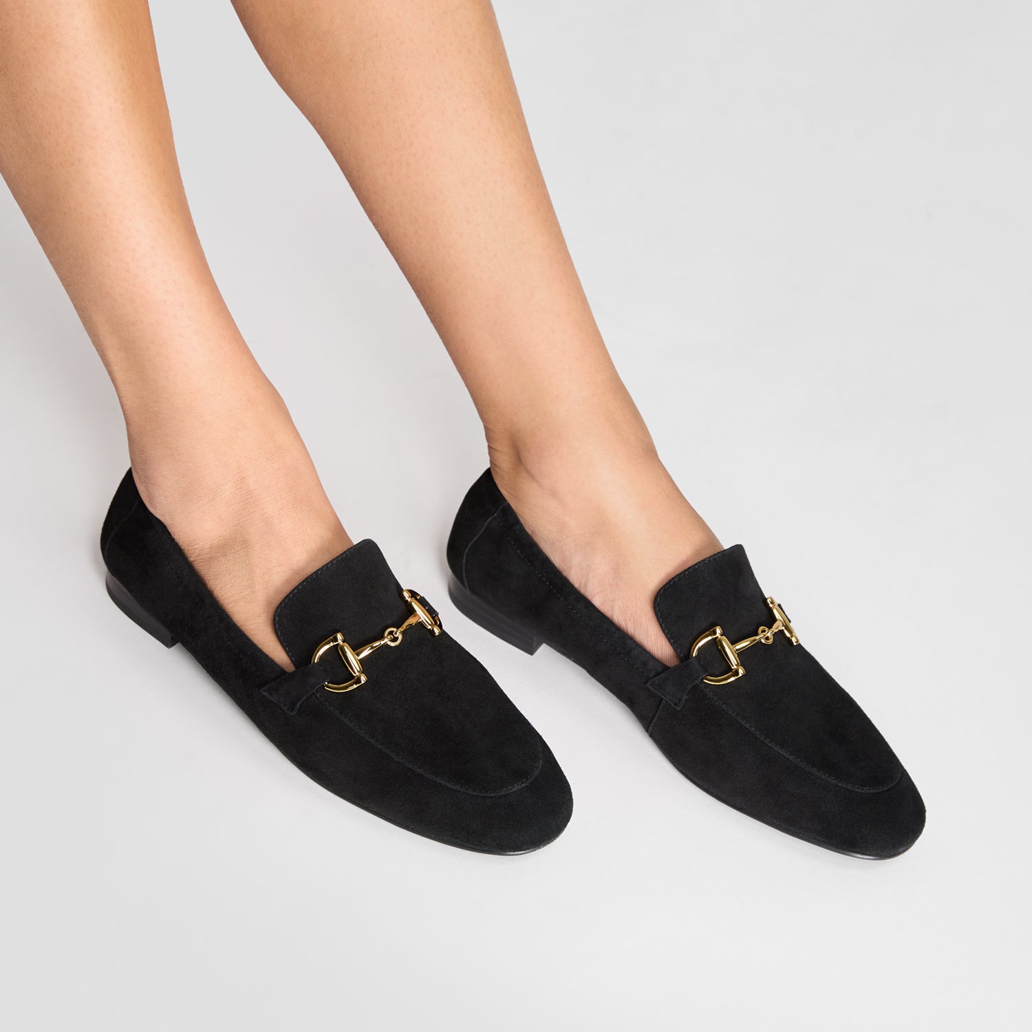 Black loafers with gold chain worn by a person on a light gray background. Round toe with 2cm heel.