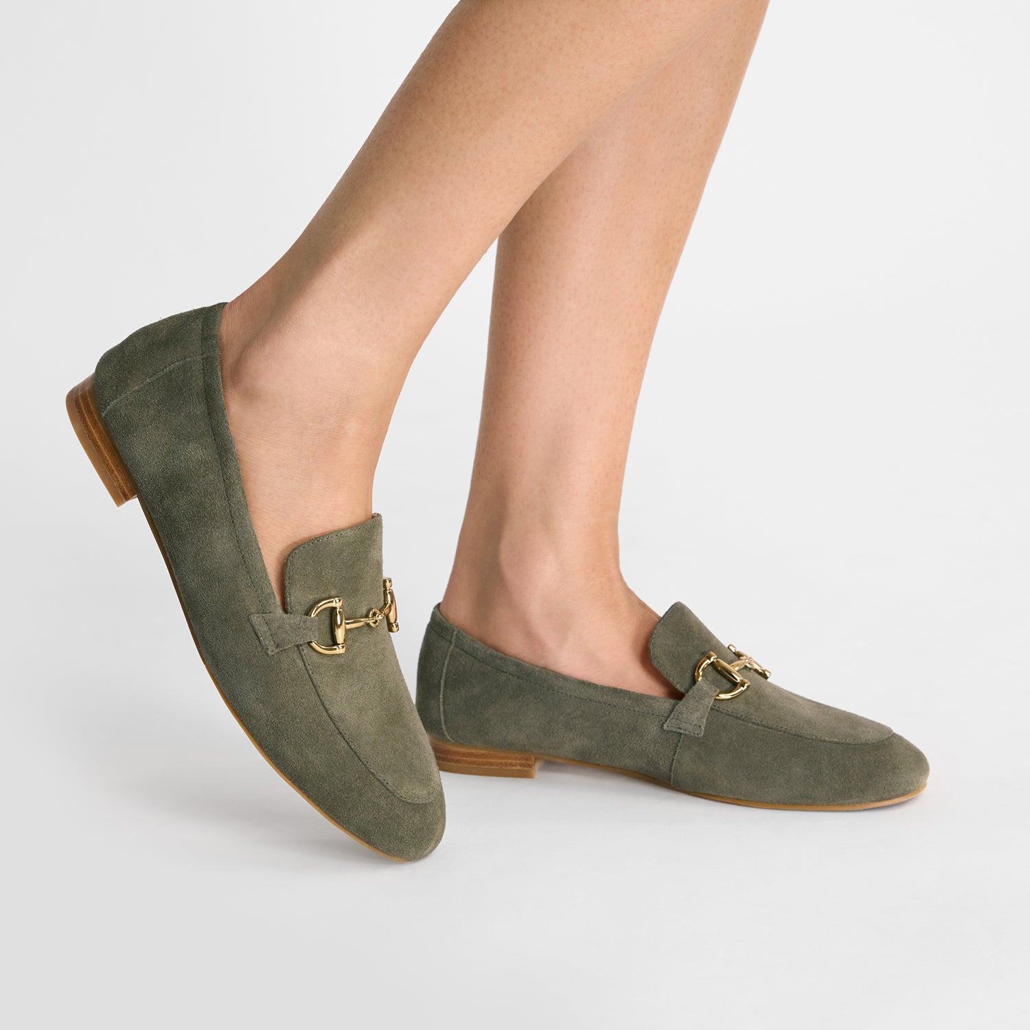 Green loafers with gold buckles worn by a person.