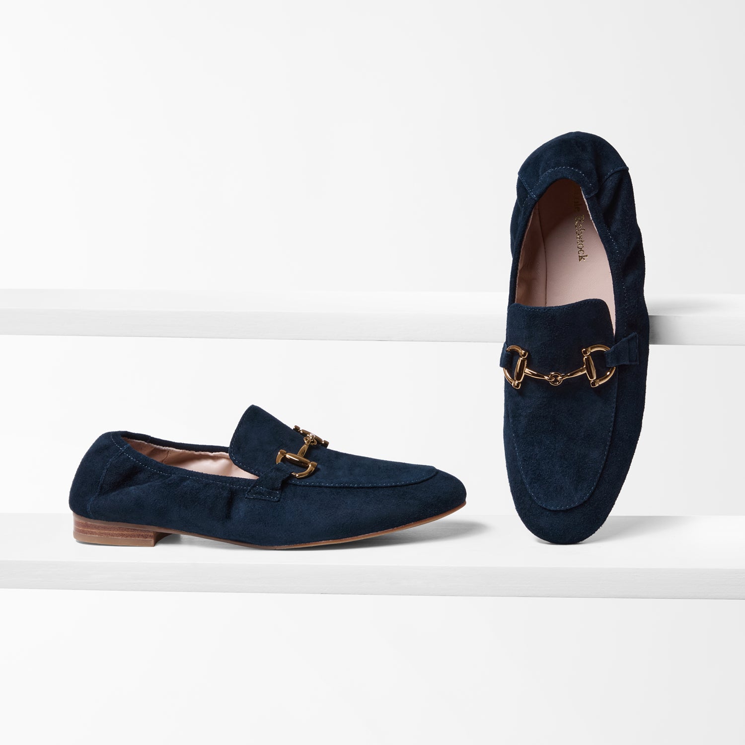 Pair of navy loafers with gold buckles on a white background
