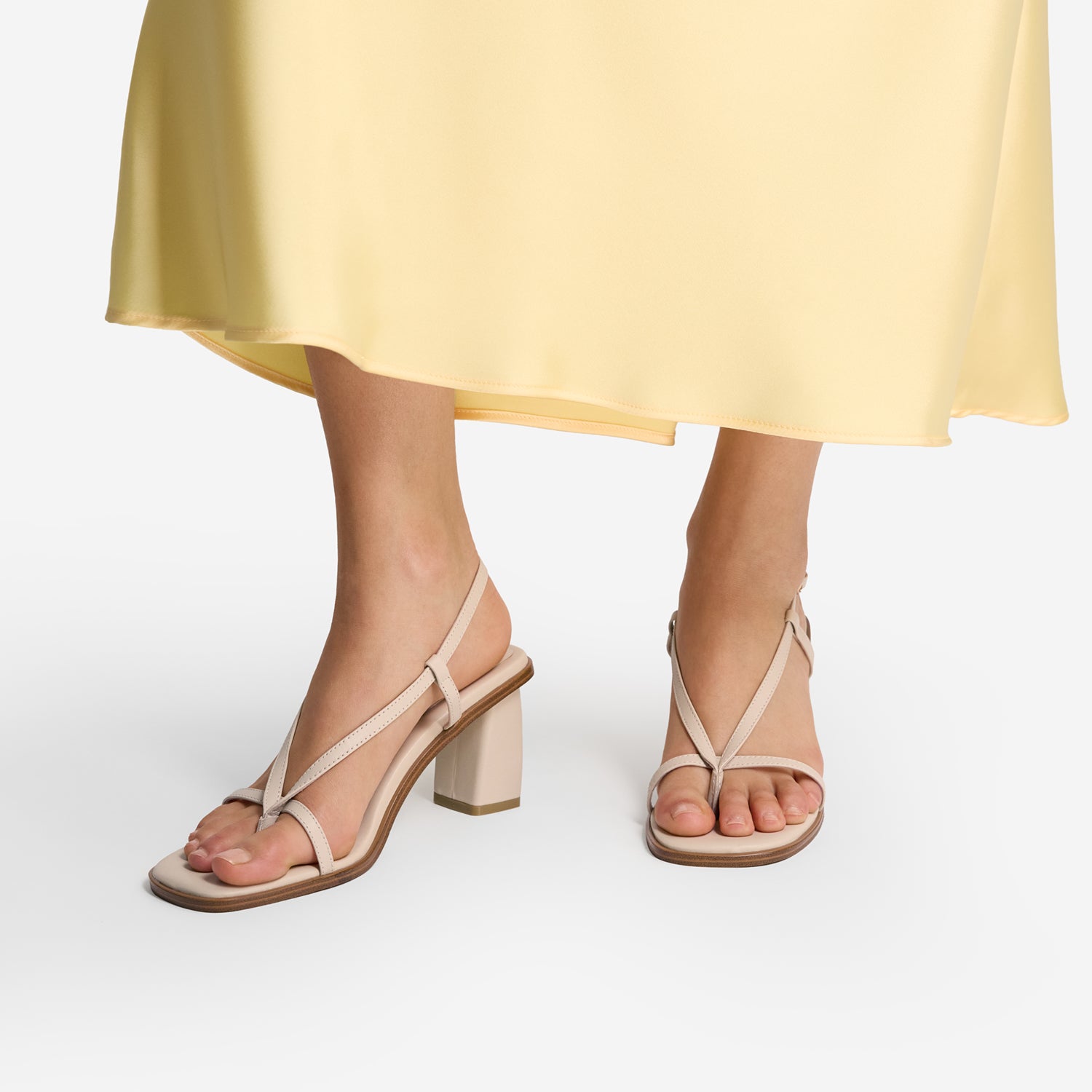 Beige sandals with square toe and strappy straps worn with a yellow skirt on a white background