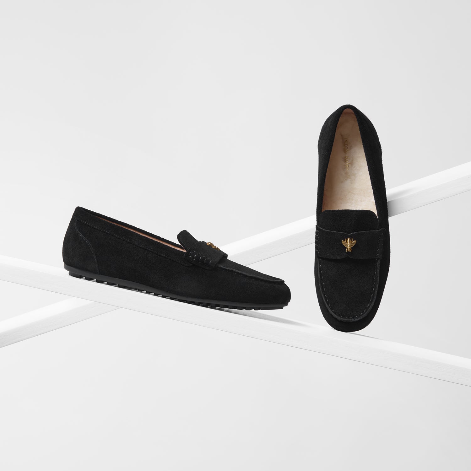 Pair of black loafers with a gold emblem and shearling wool lining on a white background