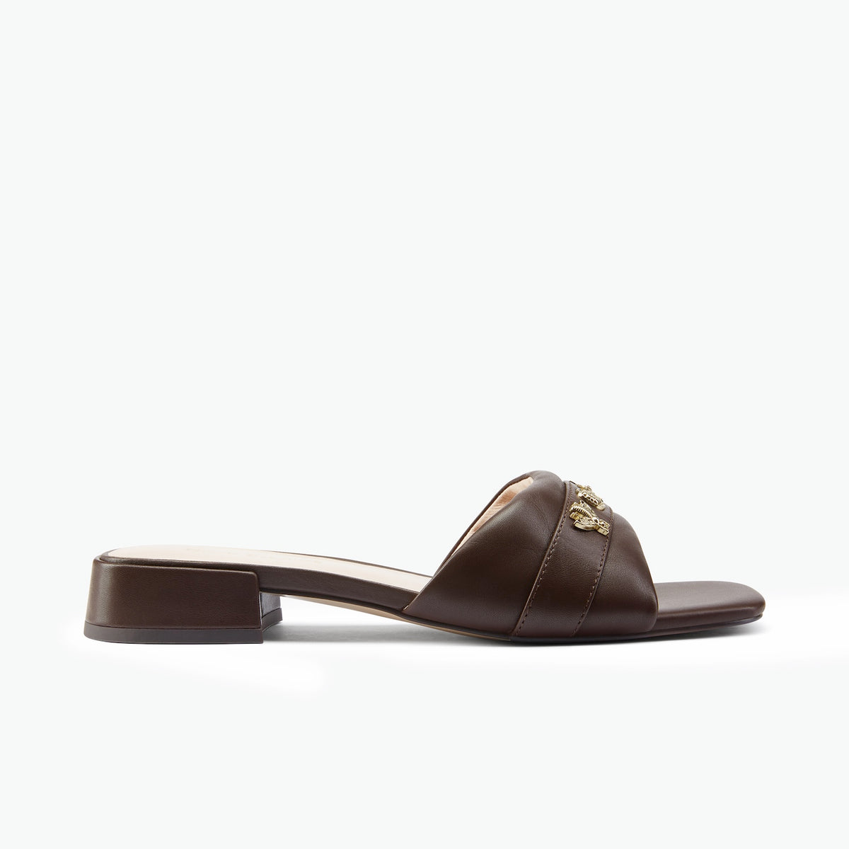 A dark brown leather slide sandal with a low block heel and a gold-tone metal logo clasp on the strap, shown in profile against a white background.