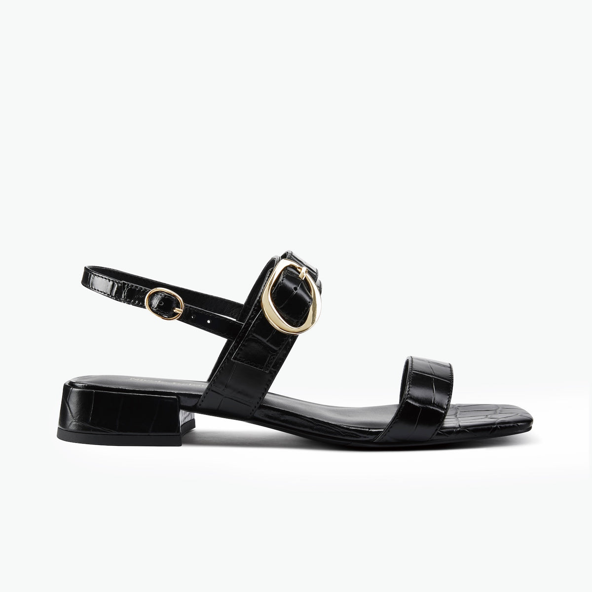 A single black flat sandal with a low block heel, a double strap design, and a prominent gold-tone circular buckle on the ankle strap, shown against a plain white background.
