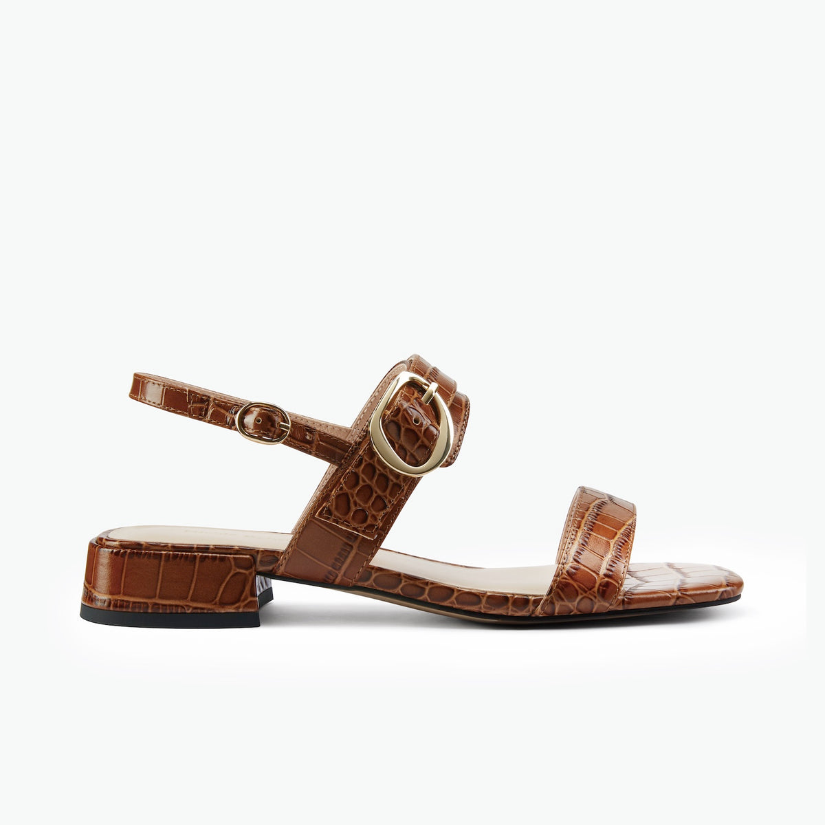 A single brown crocodile-embossed flat sandal with a low block heel, square toe, and a gold-tone buckle detail on the ankle strap, shown against a plain white background.