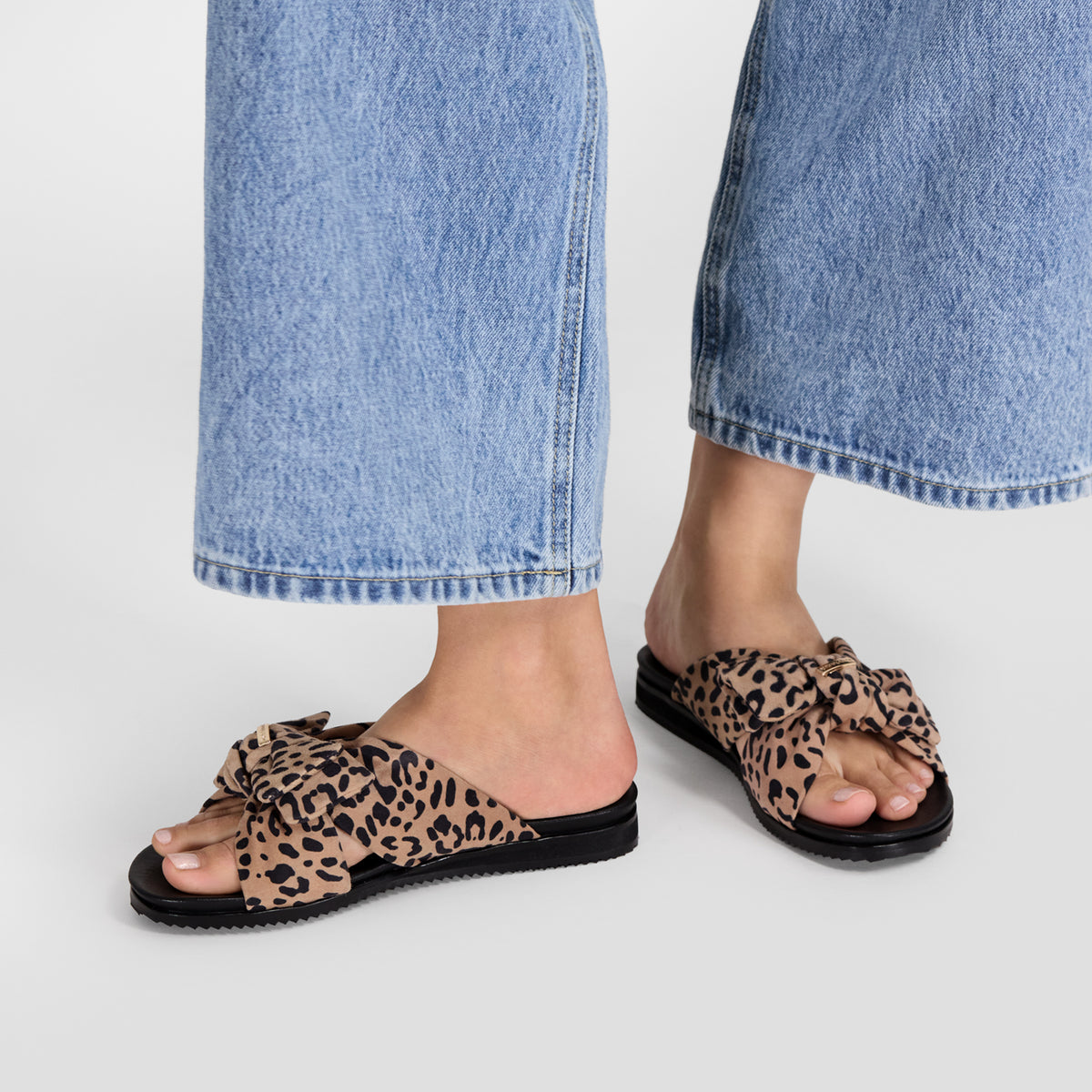 Flat leopard print slides on models feet.