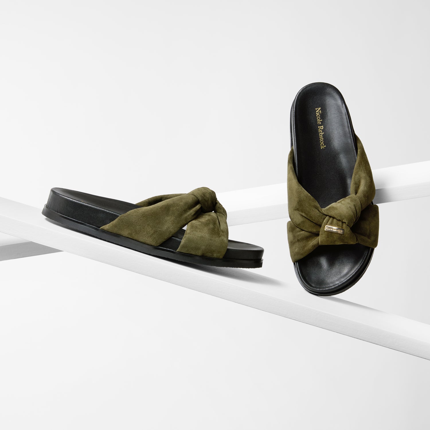 Pair of green sandals with black sole with a knot design on a white surface