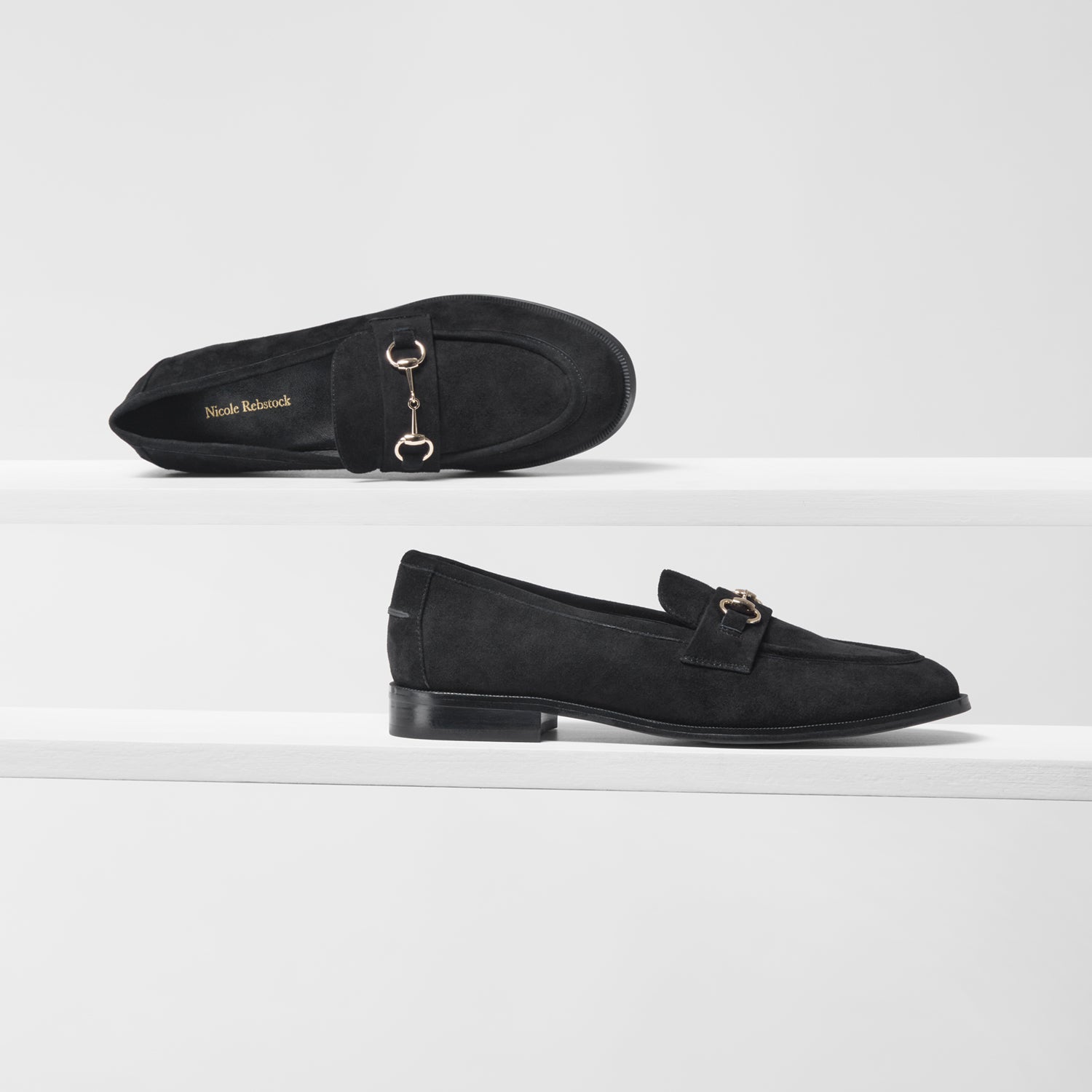 Black loafers with gold accents on a white background