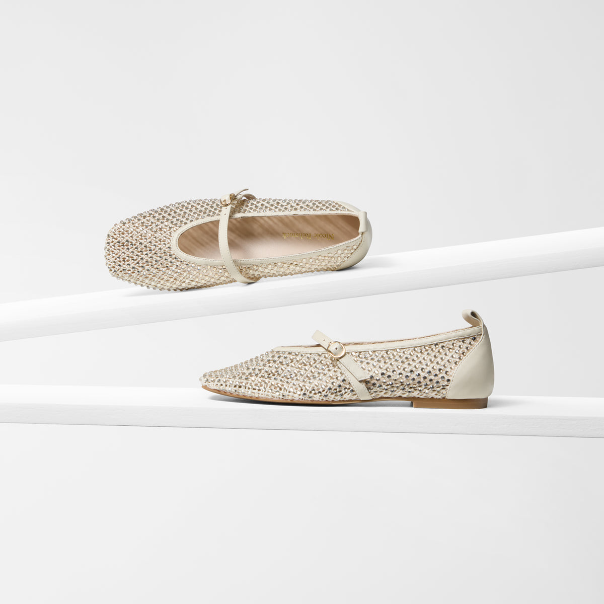 A pair of women's ballet flats in a light beige and gold woven mesh material with a small gold buckle strap, displayed on white geometric risers against a white background.