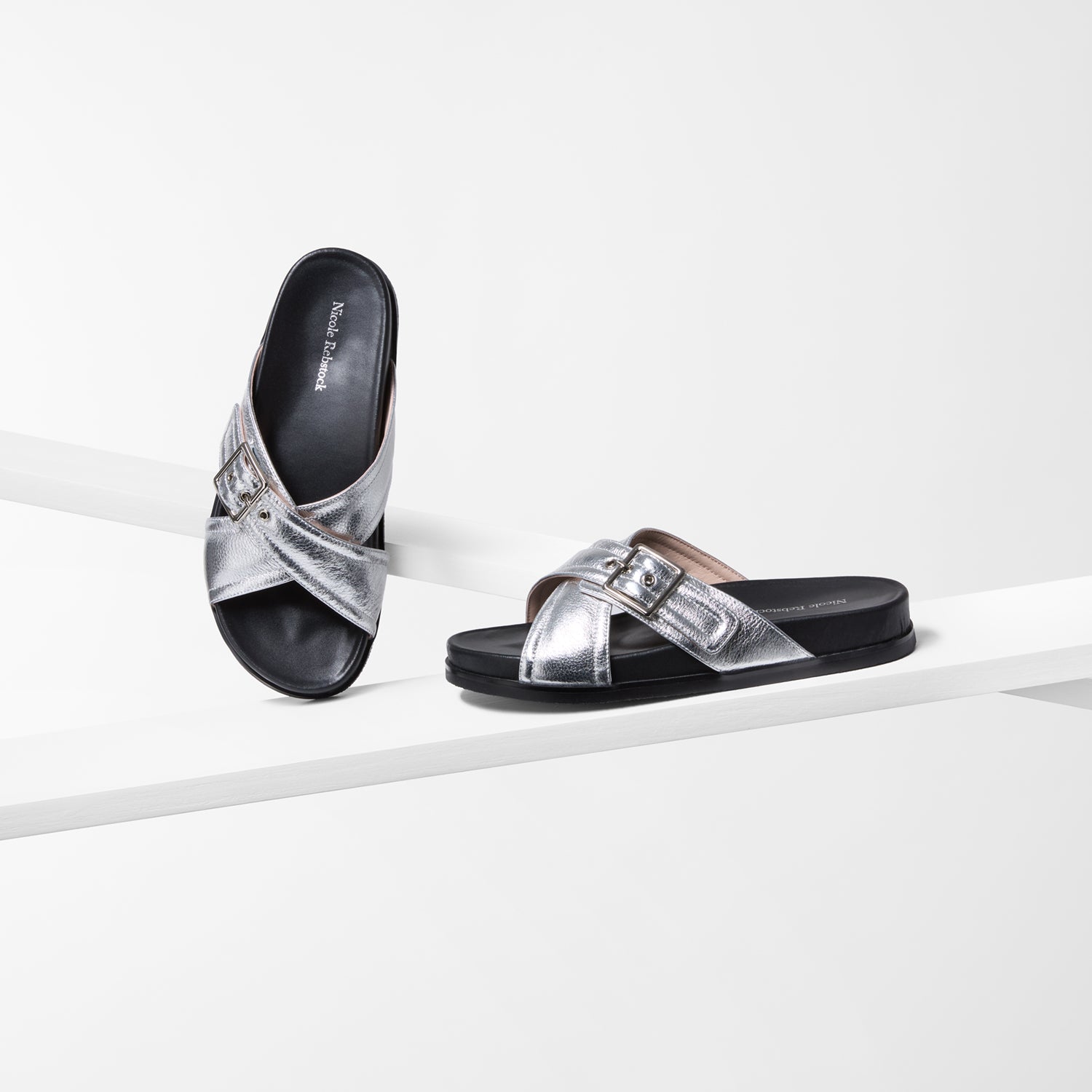 Pair of flat silver sandals with black soles on a white background