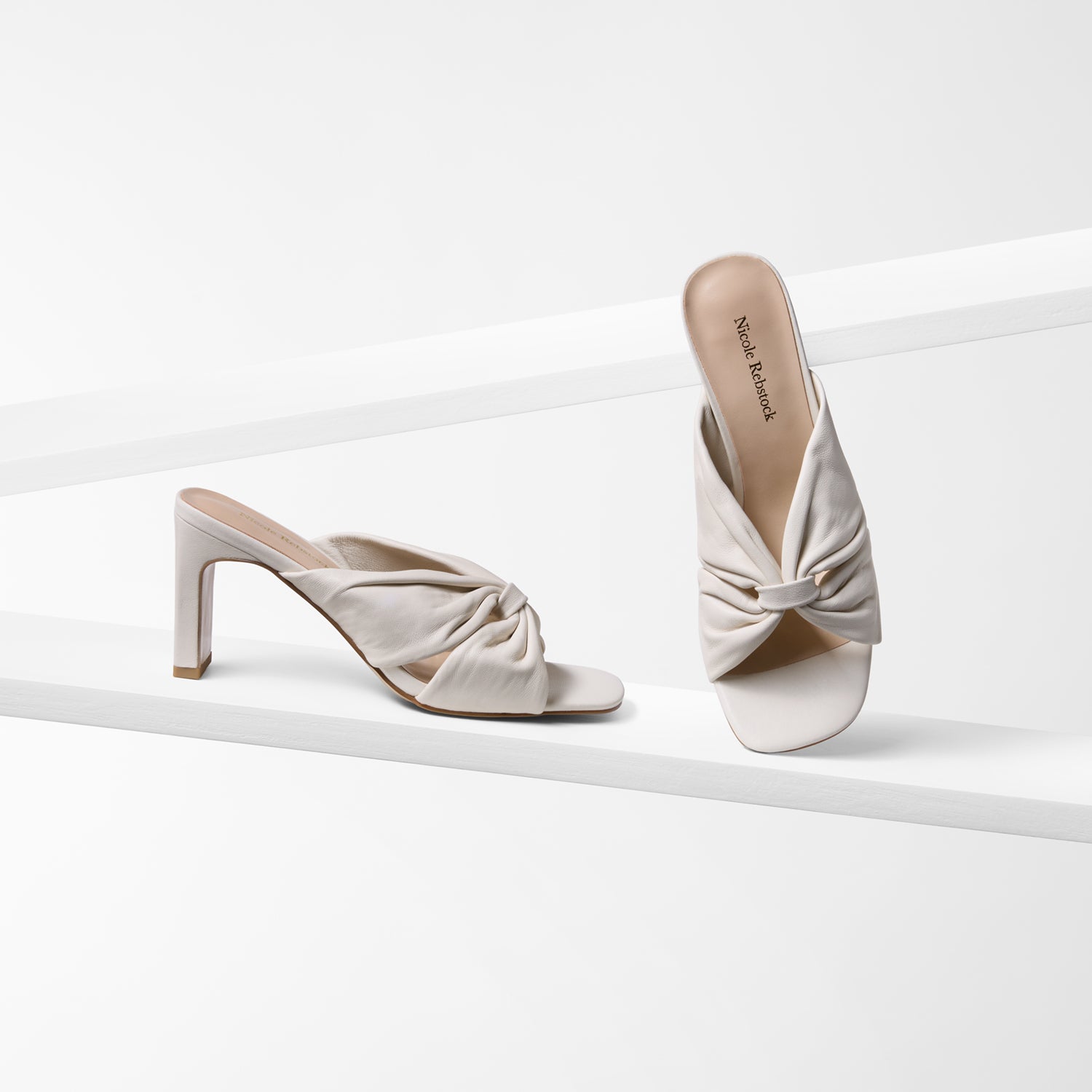 Pair of ivory leather high-heeled sandals with knotted design on a white background