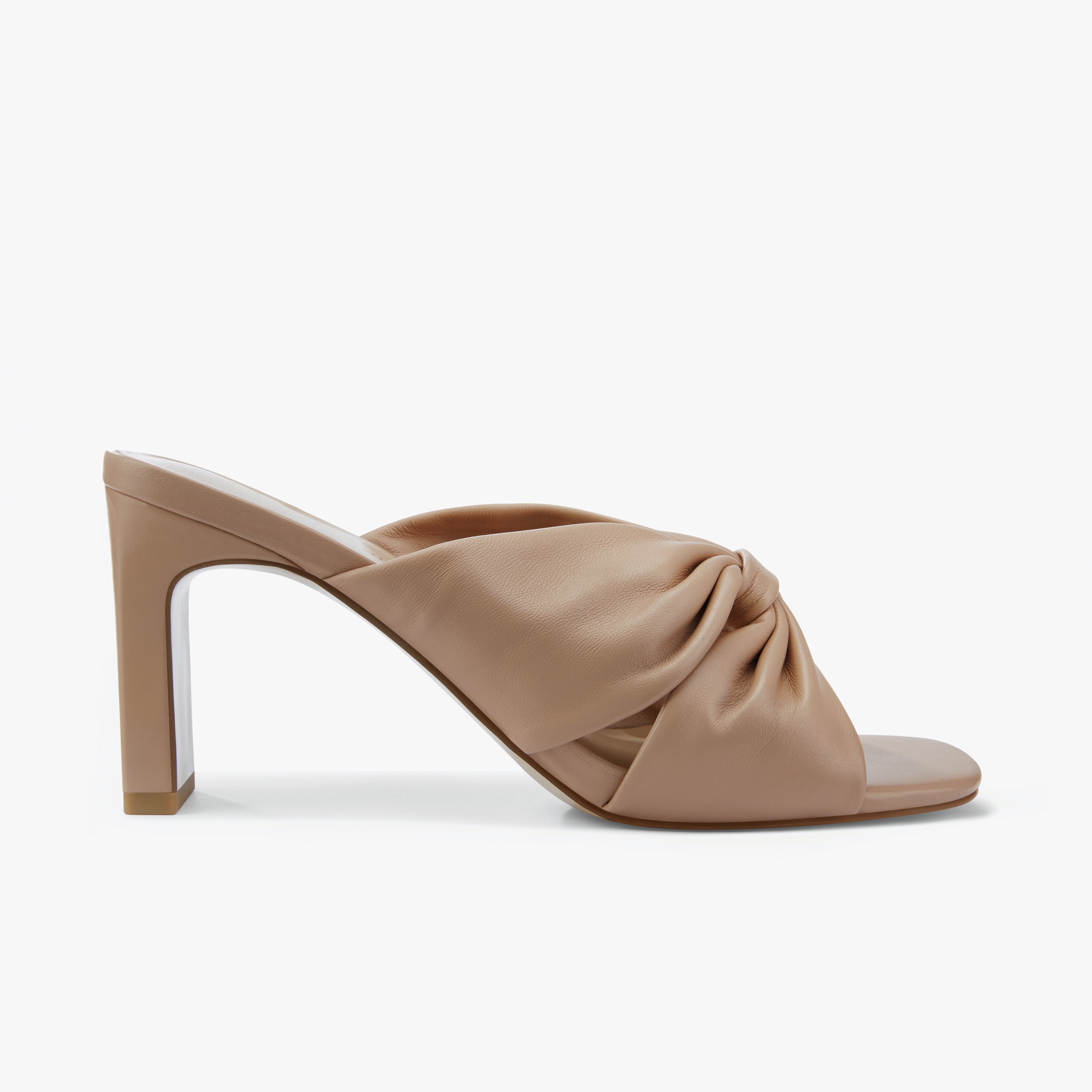 Nude high-heeled shoe with a knotted design on a white background by Nicole Rebstock