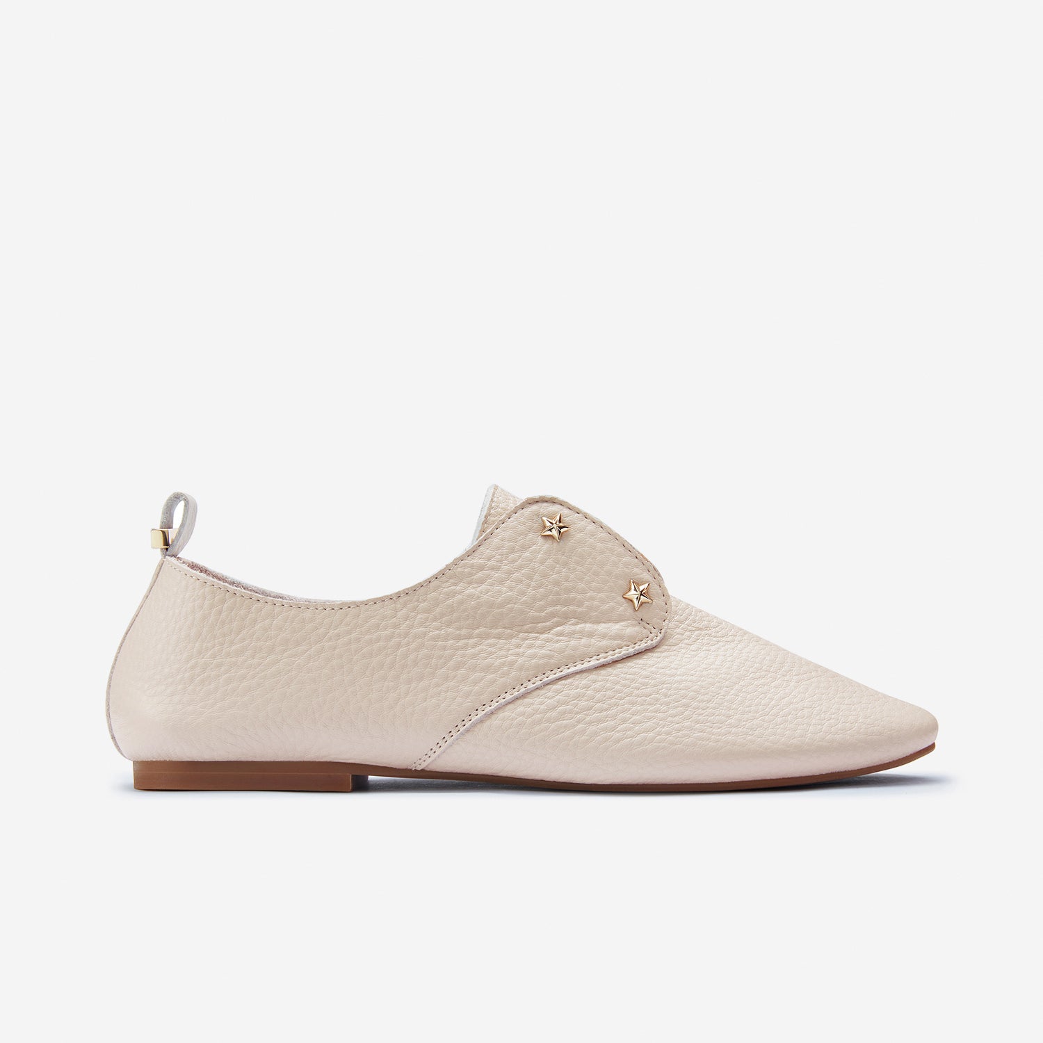 A blush pebble grain leather flat shoe with hidden tongue elastic and subtle gold hardware.