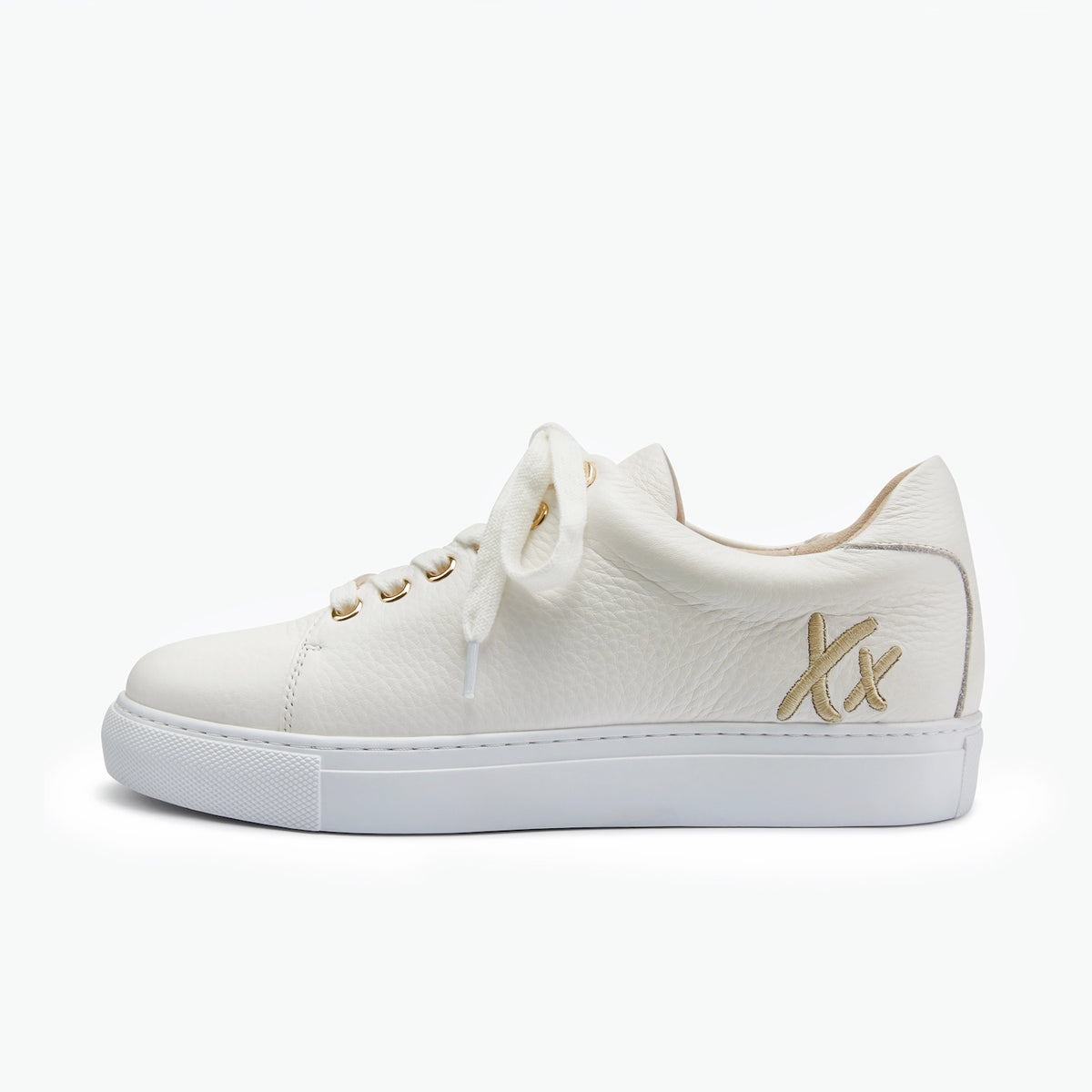 A low-top white leather sneaker with white laces, gold eyelets, and a gold 'Xx' logo on the side, shown against a plain white background.